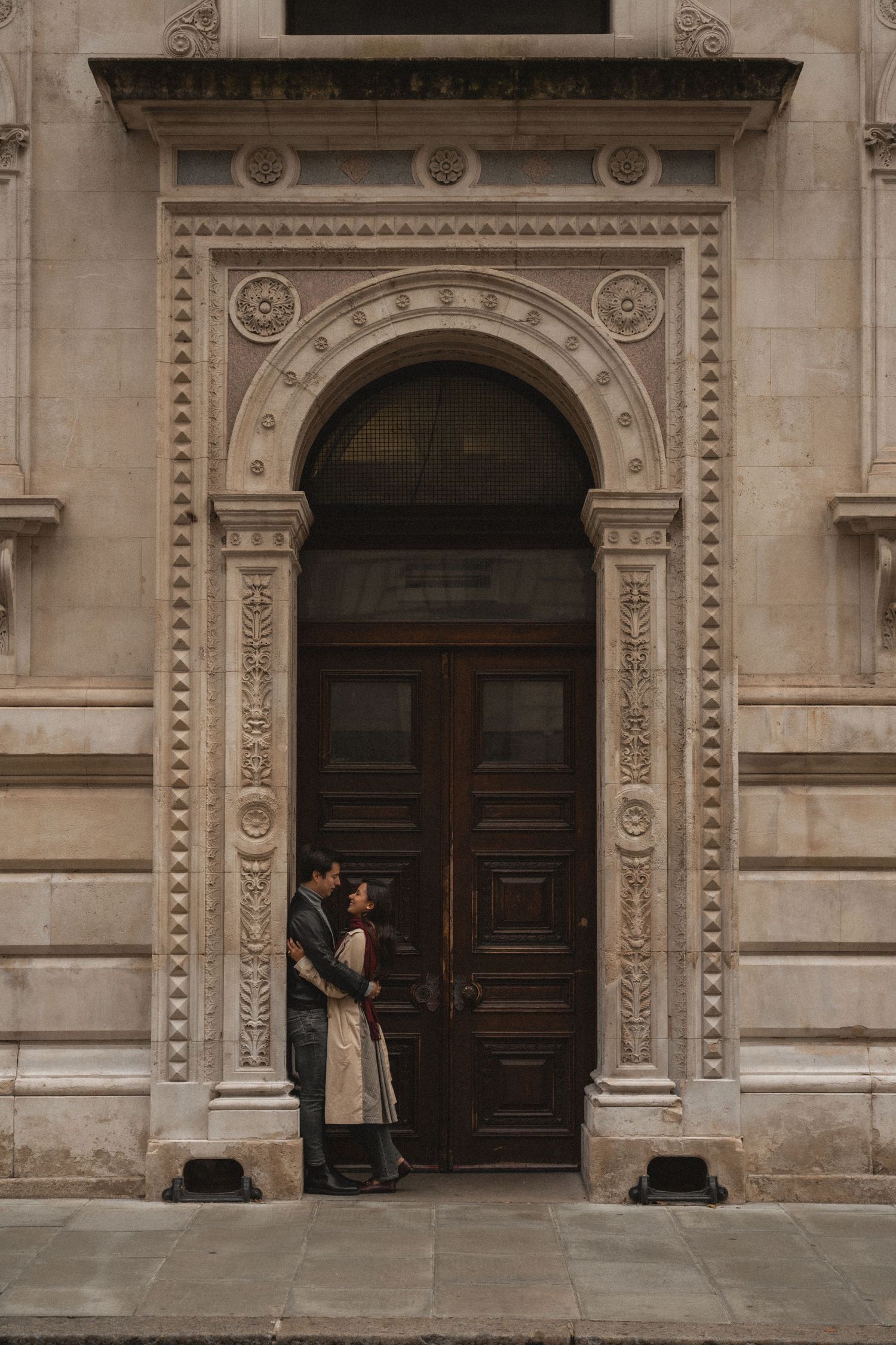Two people sit separately in ornate stone doorways of a grand historic building facade with classical architecture.