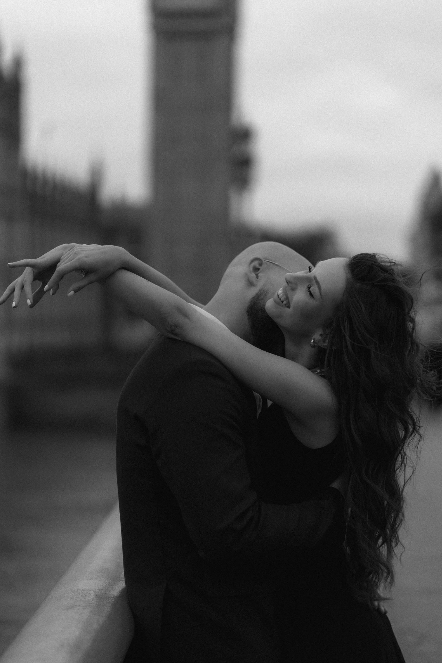 Black and white photo of a romantic couple embracing on Westminster Bridge with Big Ben in the background.