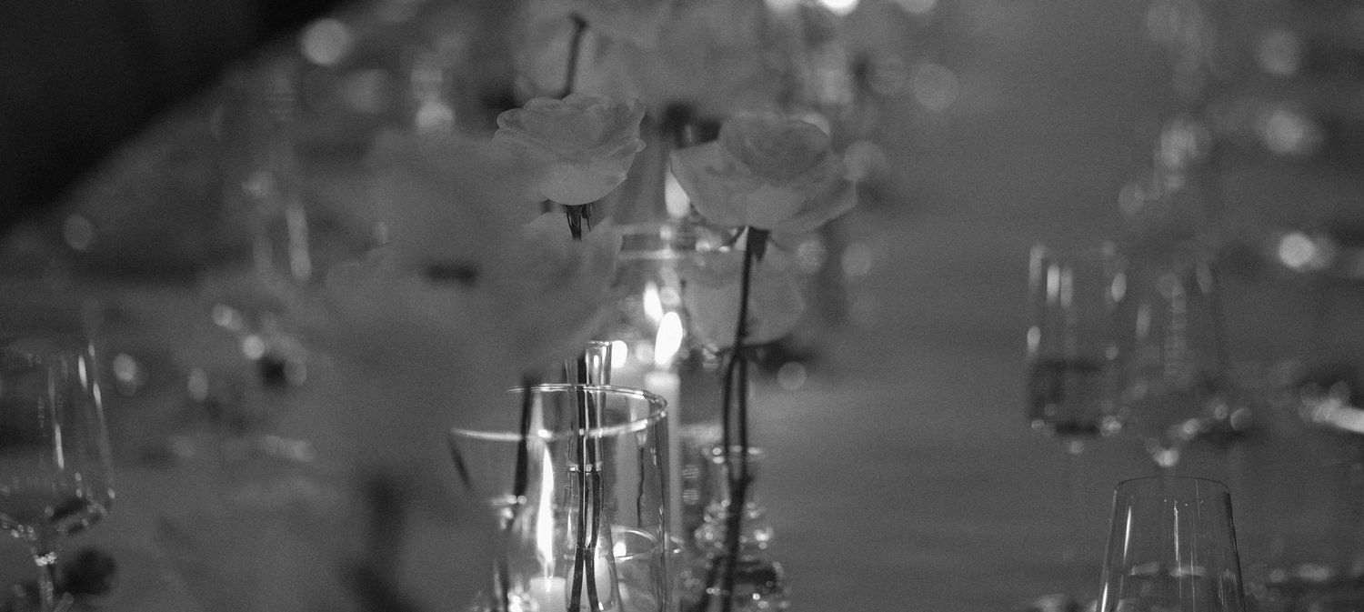 Black and white photo of delicate flowers in glass vases on an elegantly set dining table.