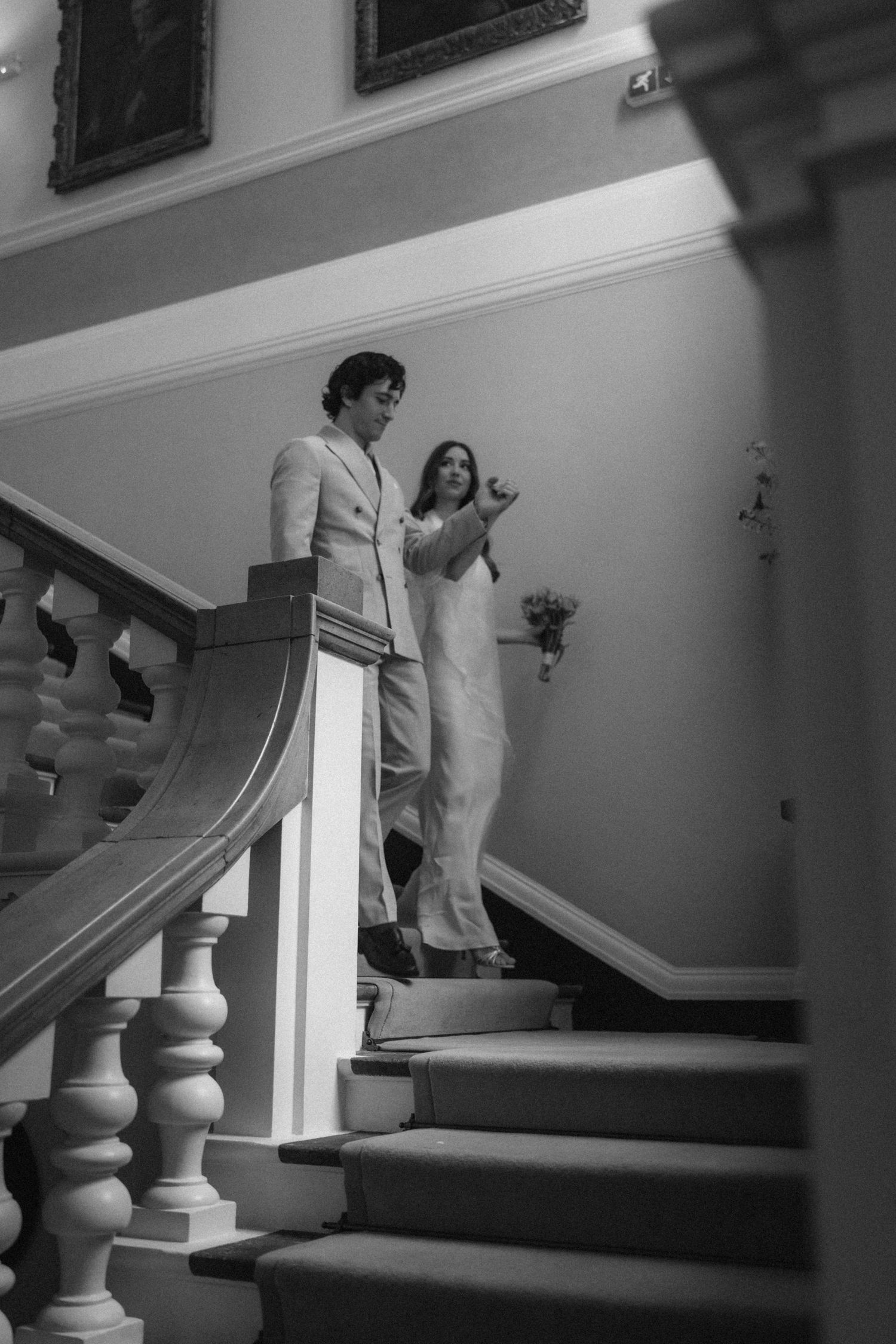 Black and white photo of a bride and groom descending an elegant staircase with ornate white balusters.