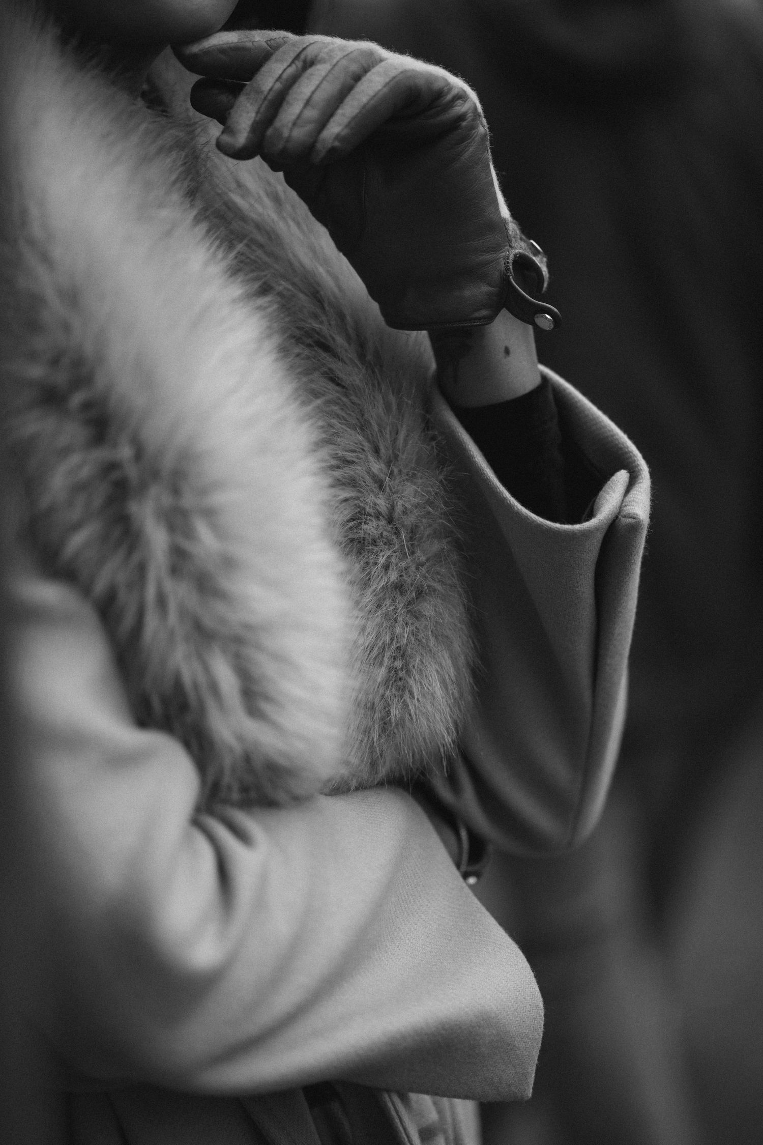 Black and white close-up photo of a person wearing a fur-trimmed coat looking to the side.
