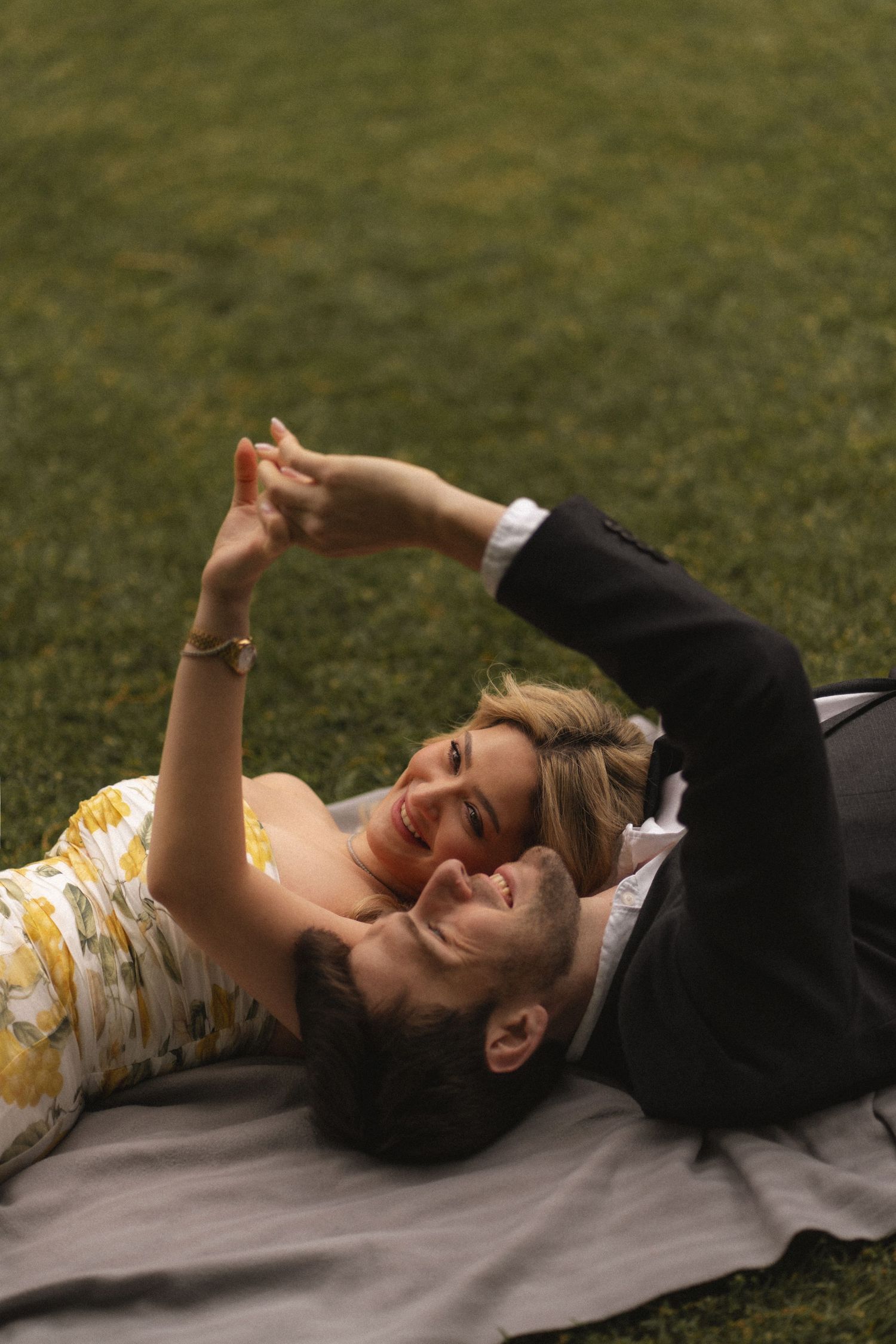 Two people lying on a blanket outdoors on grass while raising their arms in a synchronized motion.