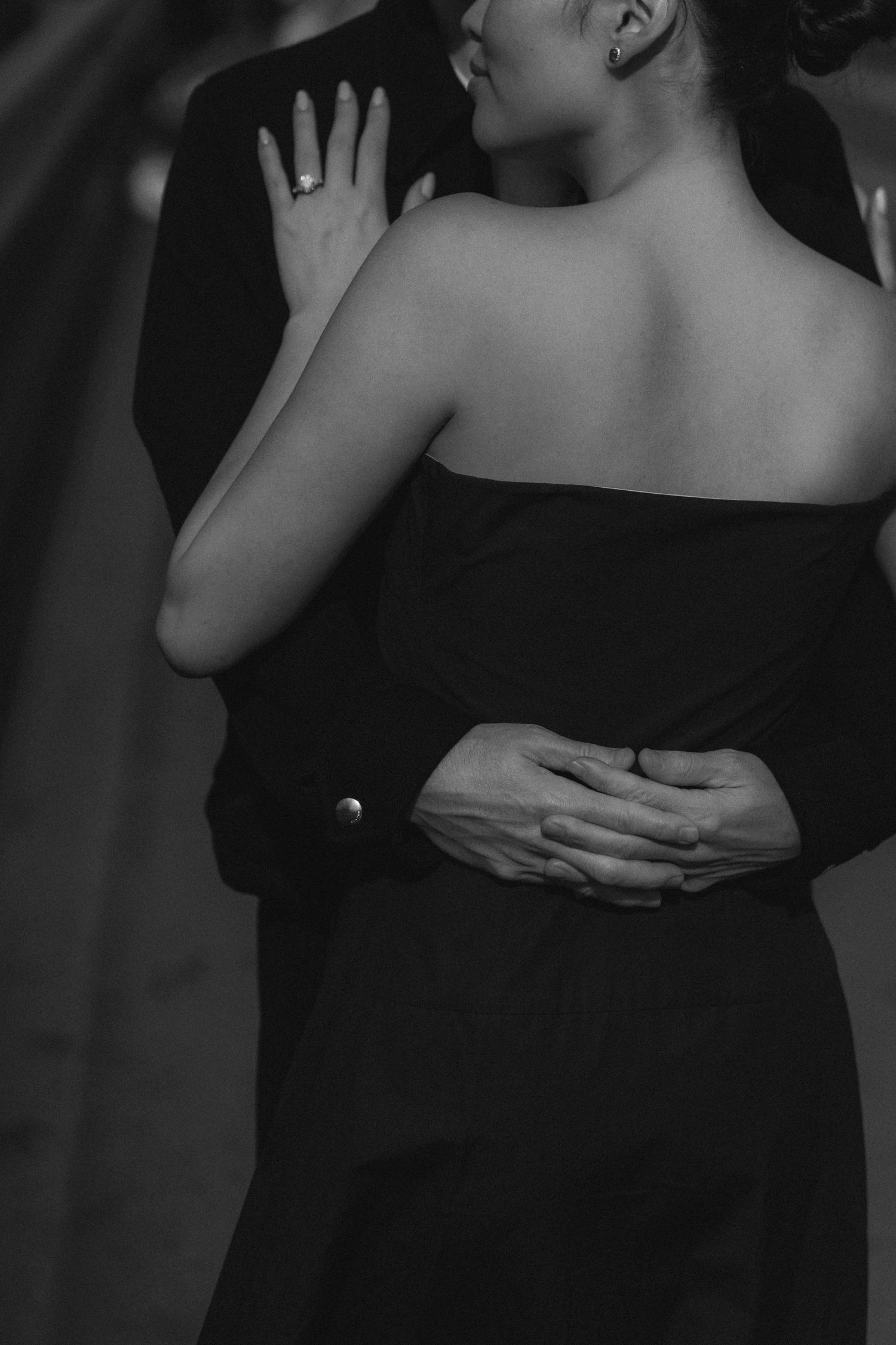A romantic black and white photo of a couple embracing in formal attire, with hands tenderly placed on each other.