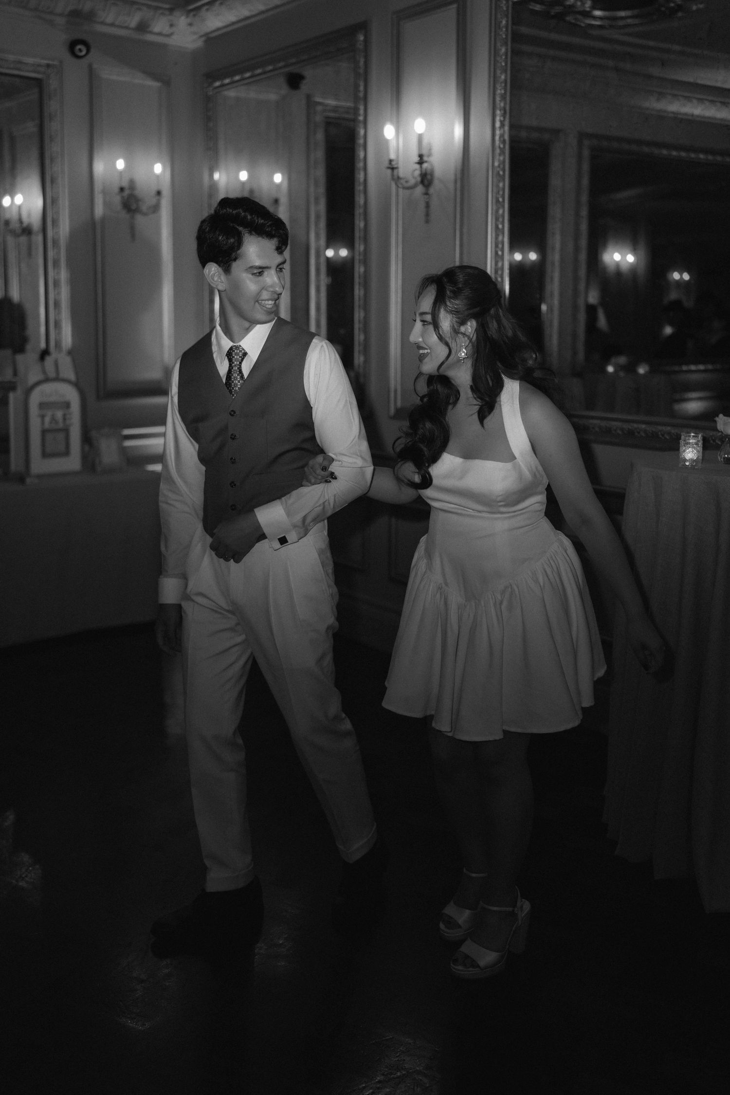 Black and white photo of a couple dancing elegantly at a formal wedding reception in a grand ballroom.