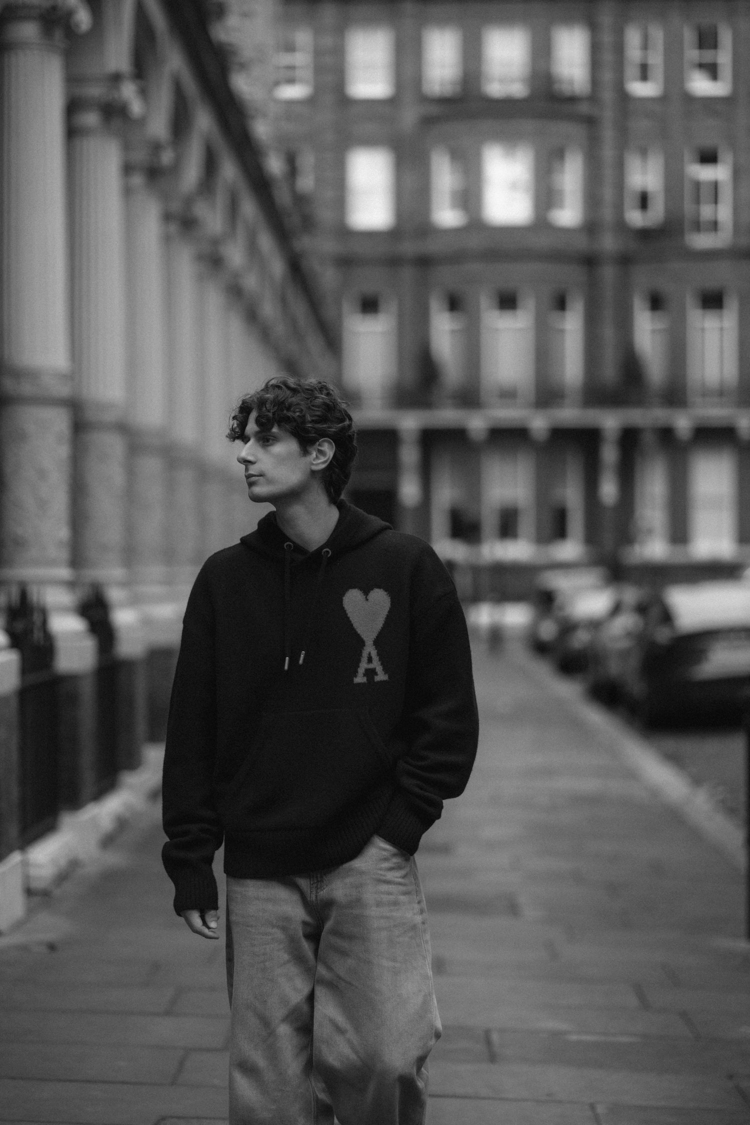 A black and white photo series showing someone in dark clothing walking along a city sidewalk near historic buildings.