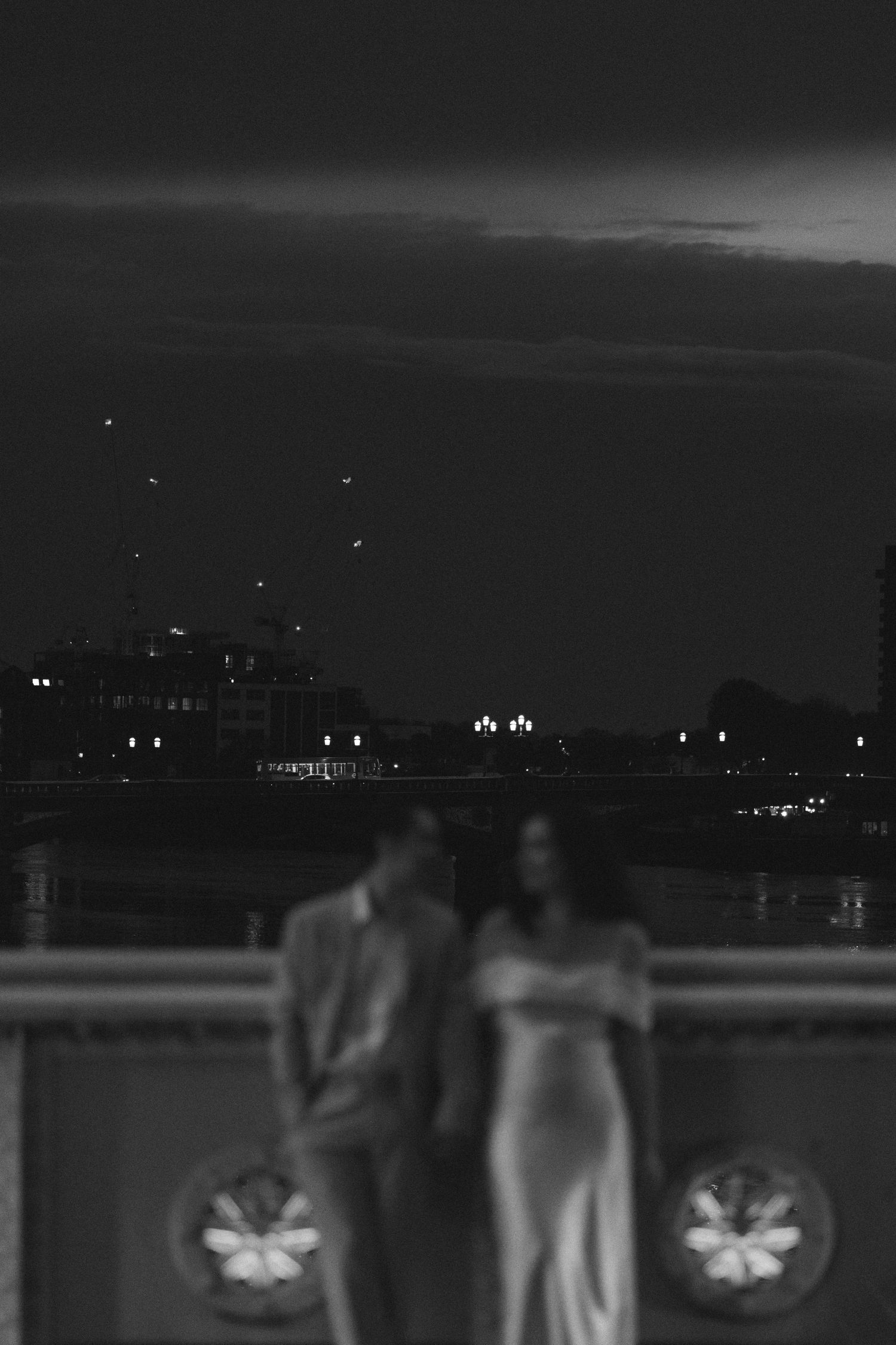 A black and white nighttime cityscape with silhouettes visible against illuminated buildings in the background.