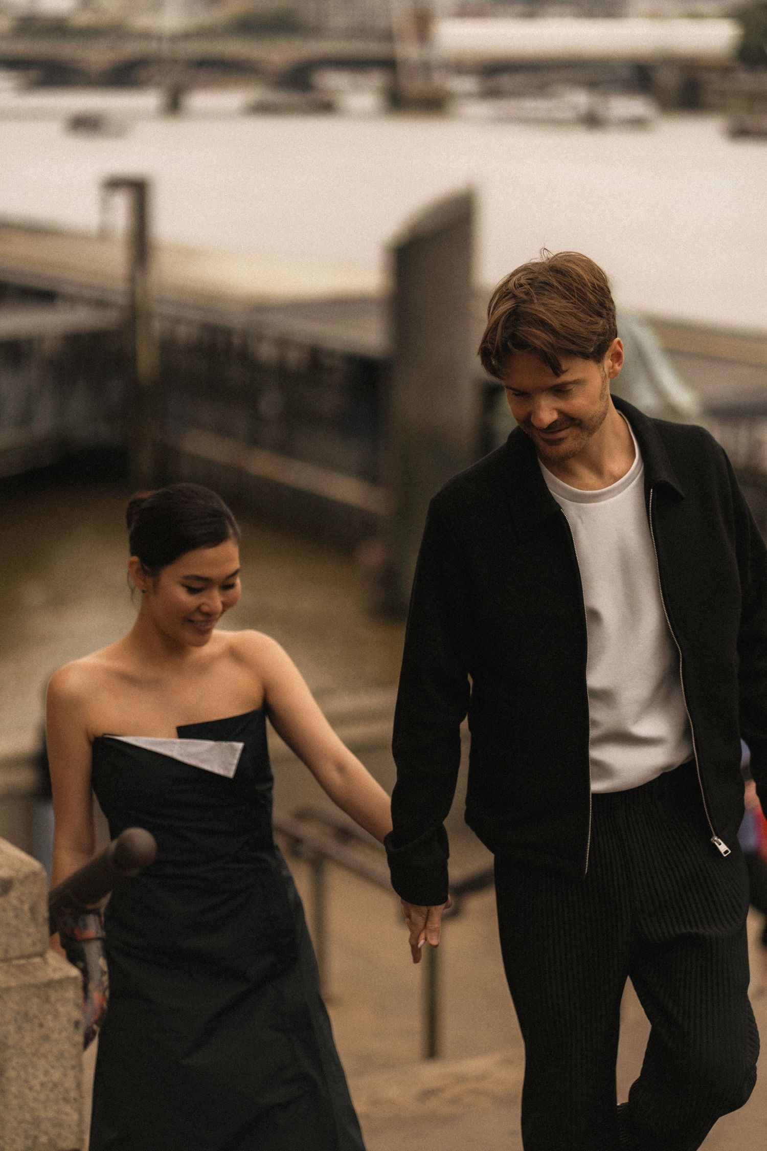 A couple in formal black and white attire walks together in a romantic outdoor setting.