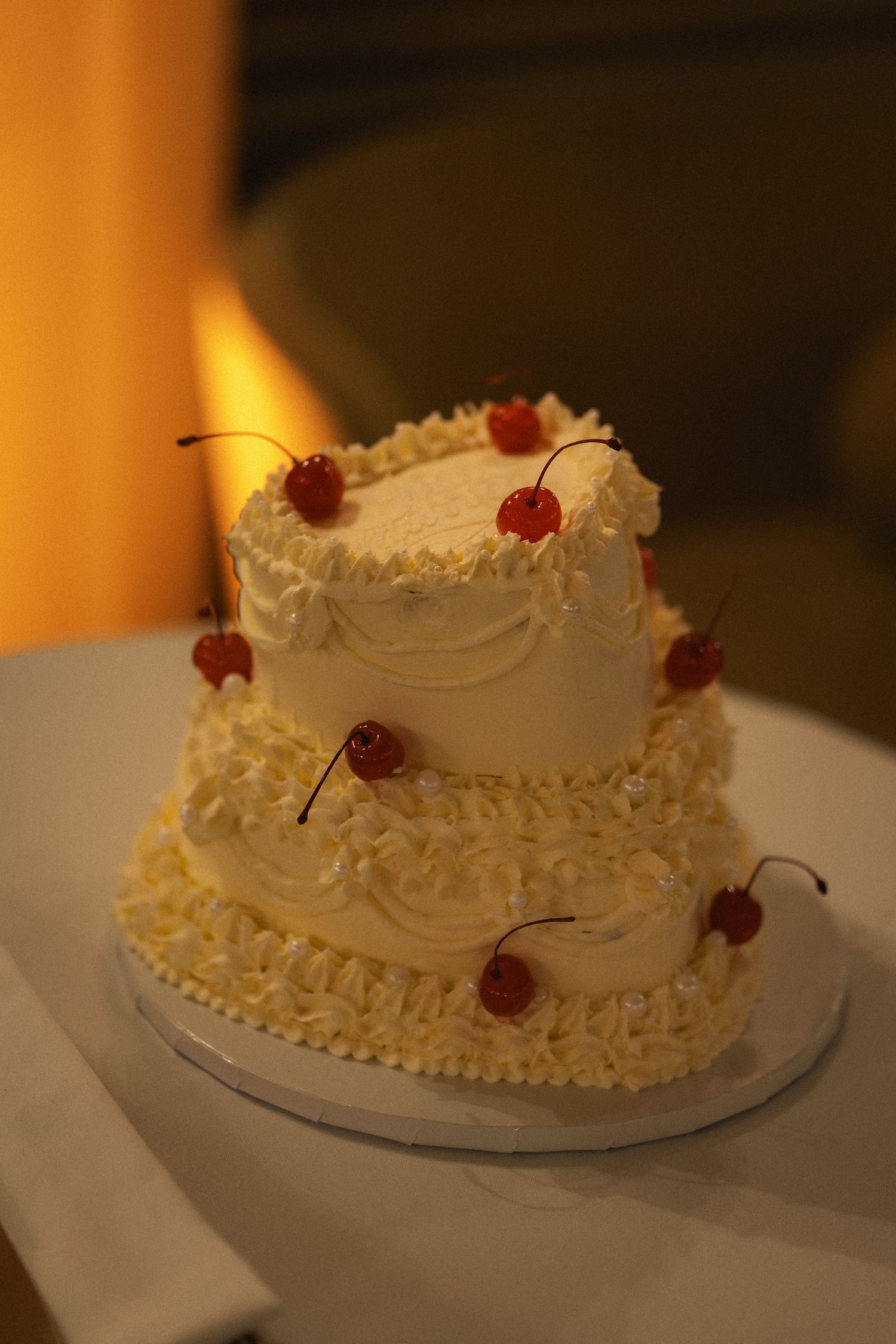 Two-tier white frosted wedding cake decorated with maraschino cherries and piped cream rosettes on a white stand.