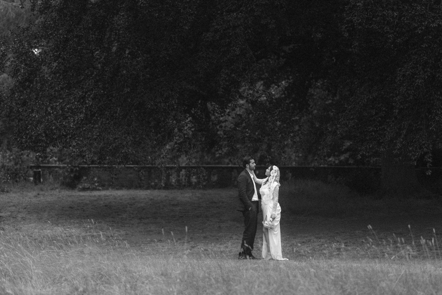 Black and white photo of a bride and groom standing together in a lush green field on their wedding day.