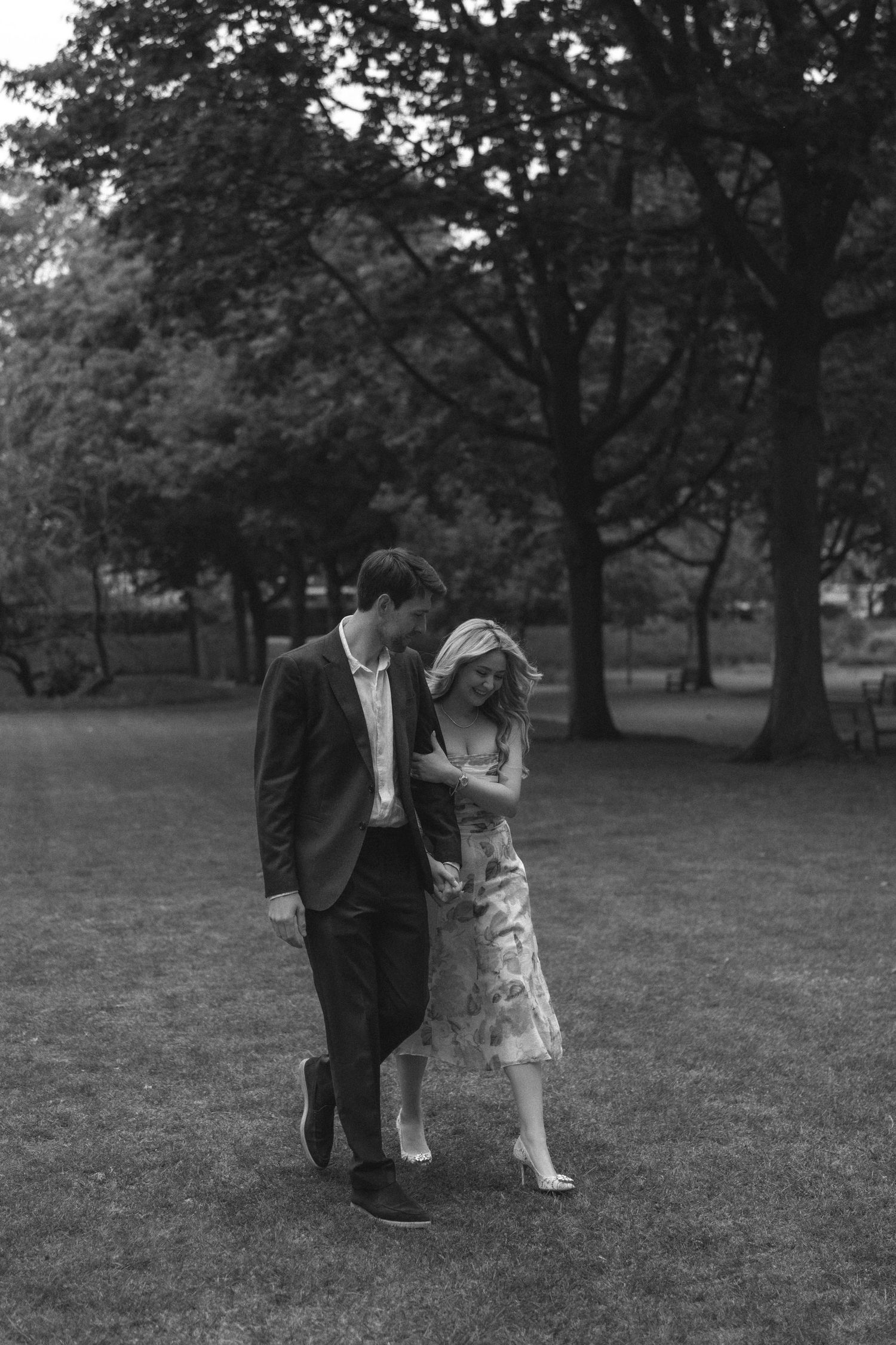 A black and white photo series shows a couple dancing playfully in a park setting with trees in the background.