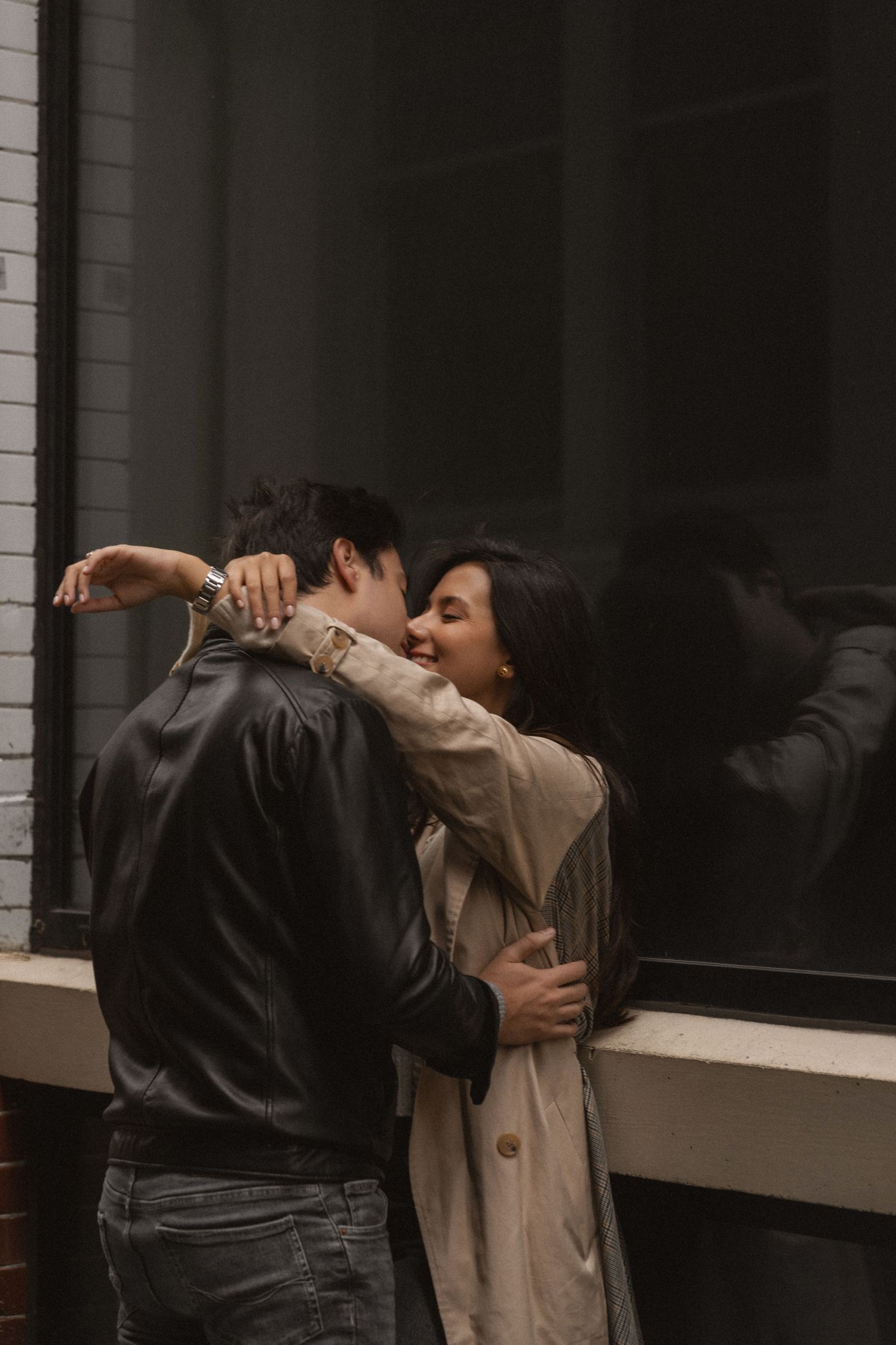A couple embraces in a romantic dance pose against a dark background with window light.