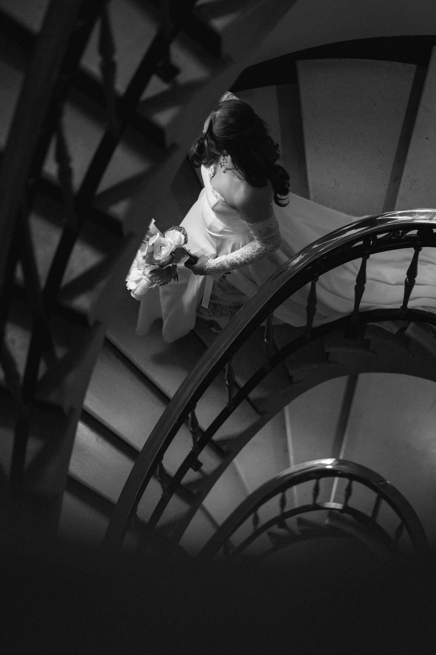 A black and white photo series showing a person in white descending a spiral staircase, creating a dramatic shadowy effect.