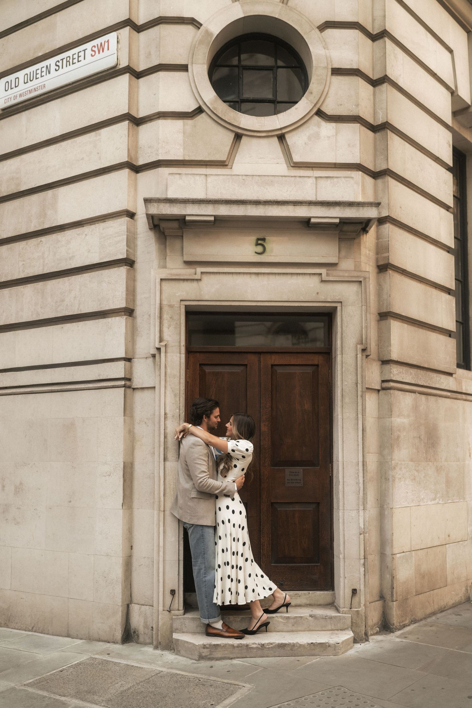 Couple embracing in a doorway on Old Queen Street SW1, London, wearing stylish outfits in a romantic urban setting.
