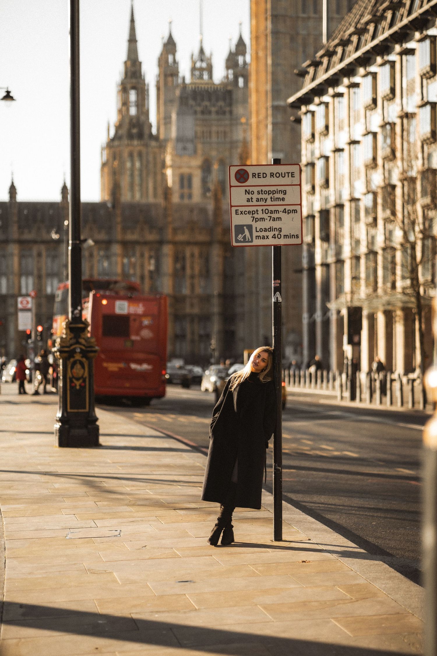 A street scene in Edinburgh with gothic architecture, red bus, and figure waiting at a bus stop in warm evening light.