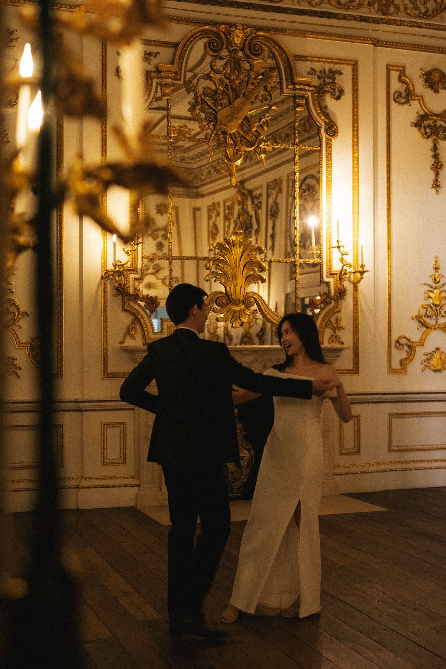 A couple dances elegantly in a luxurious ballroom with ornate gold baroque wall decorations and candlelit sconces.