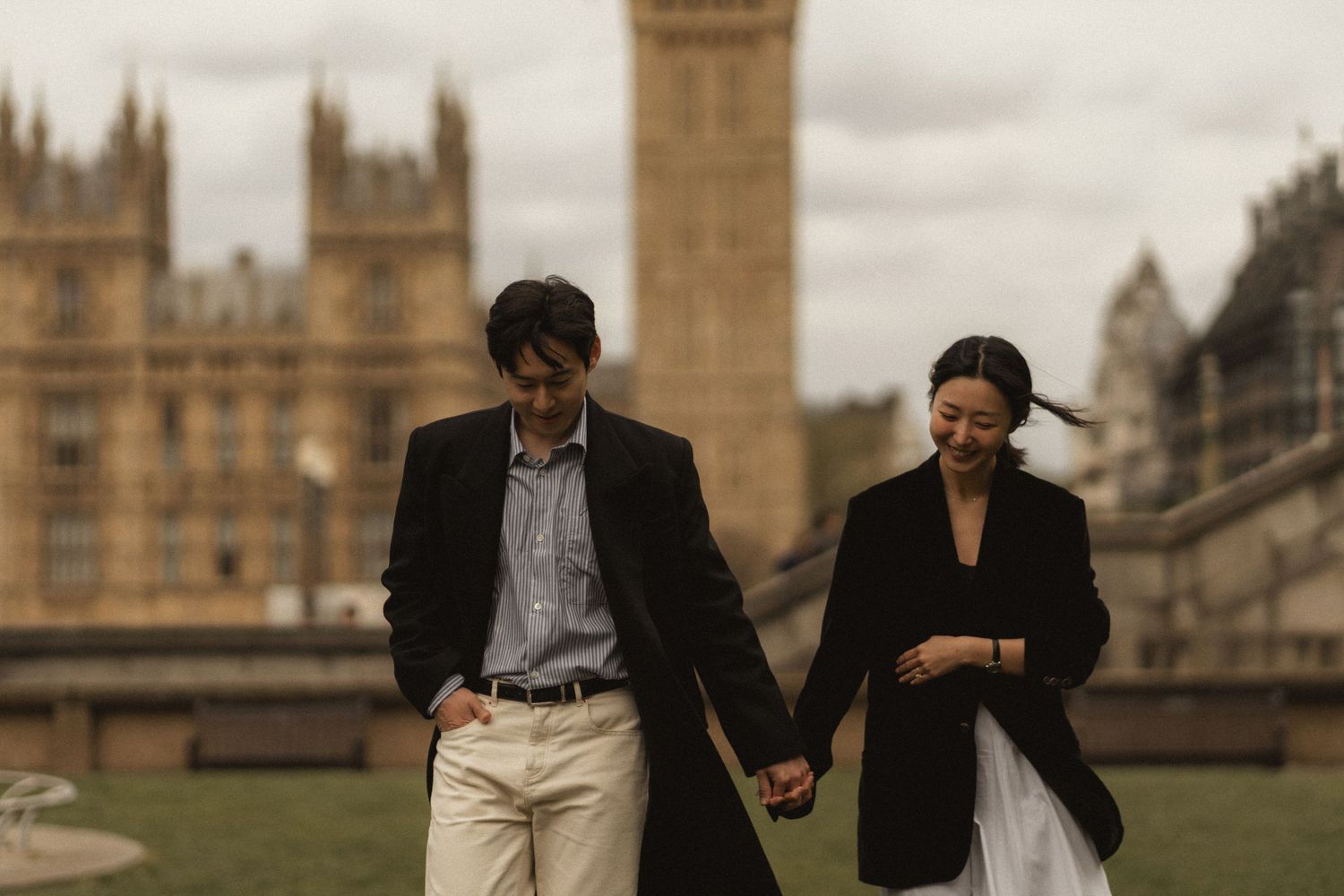 Two people walk past the historic Houses of Parliament and Big Ben in London on an overcast day.
