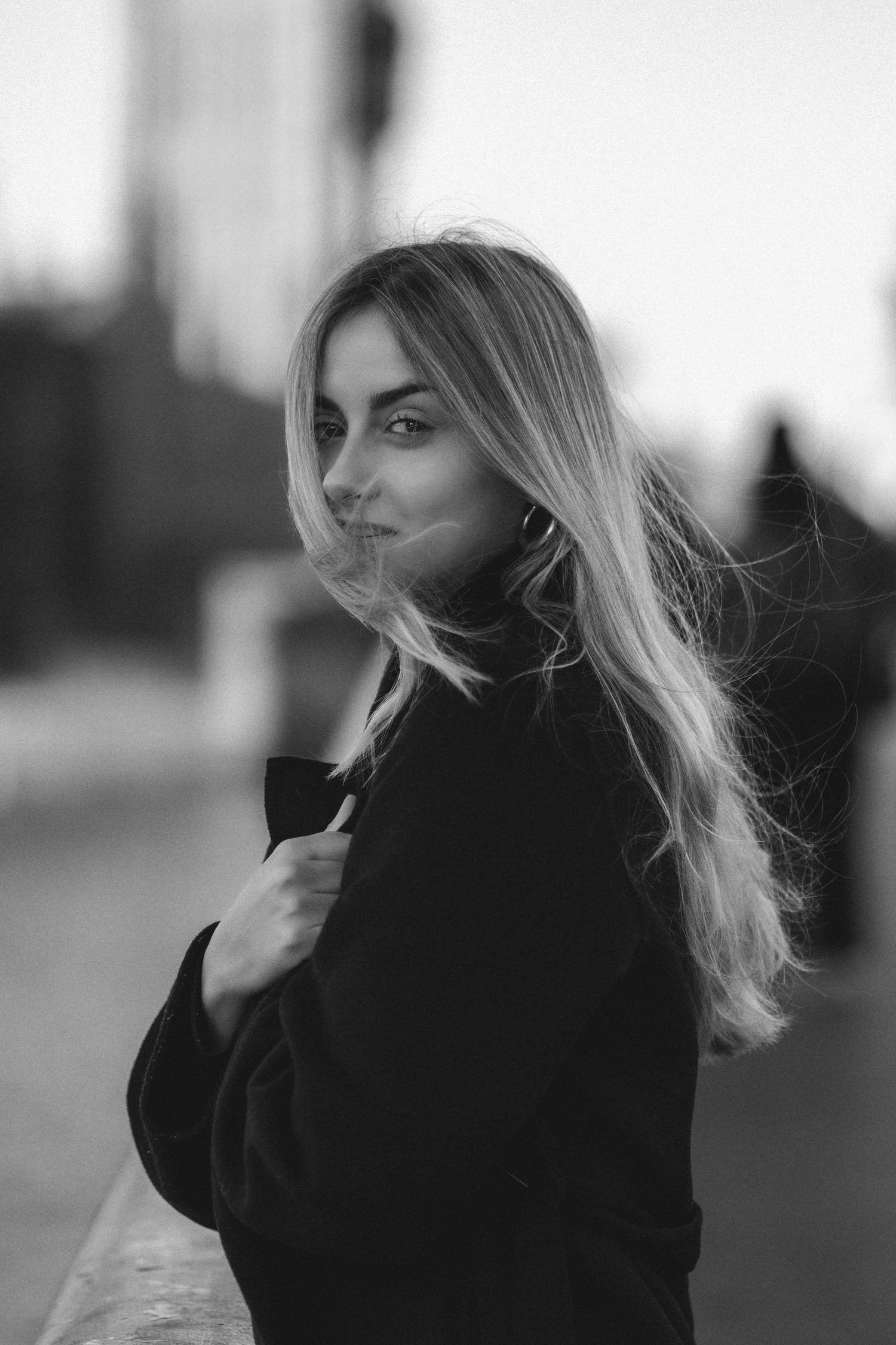 Black and white portrait series of a person with flowing blonde hair wearing a dark coat in moody lighting.