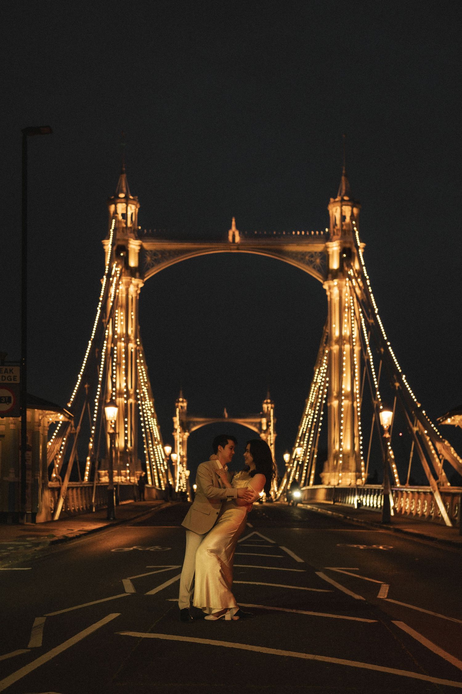 A romantic nighttime scene on Albert Bridge in London with illuminated towers and string lights creating a magical atmosphere.