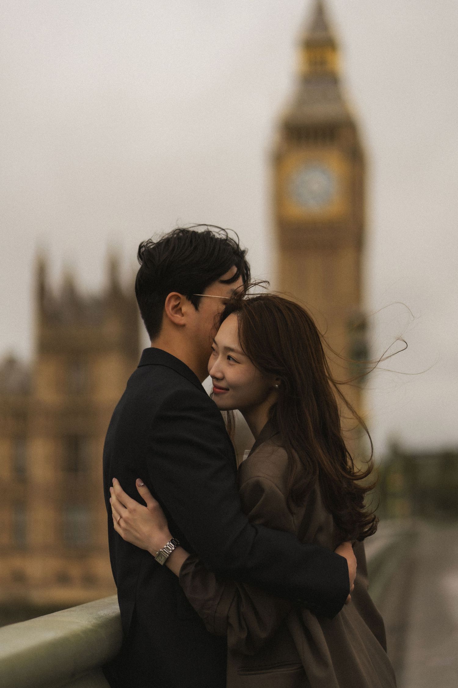 A romantic couple embraces in front of Big Ben and the Houses of Parliament in London during golden hour.