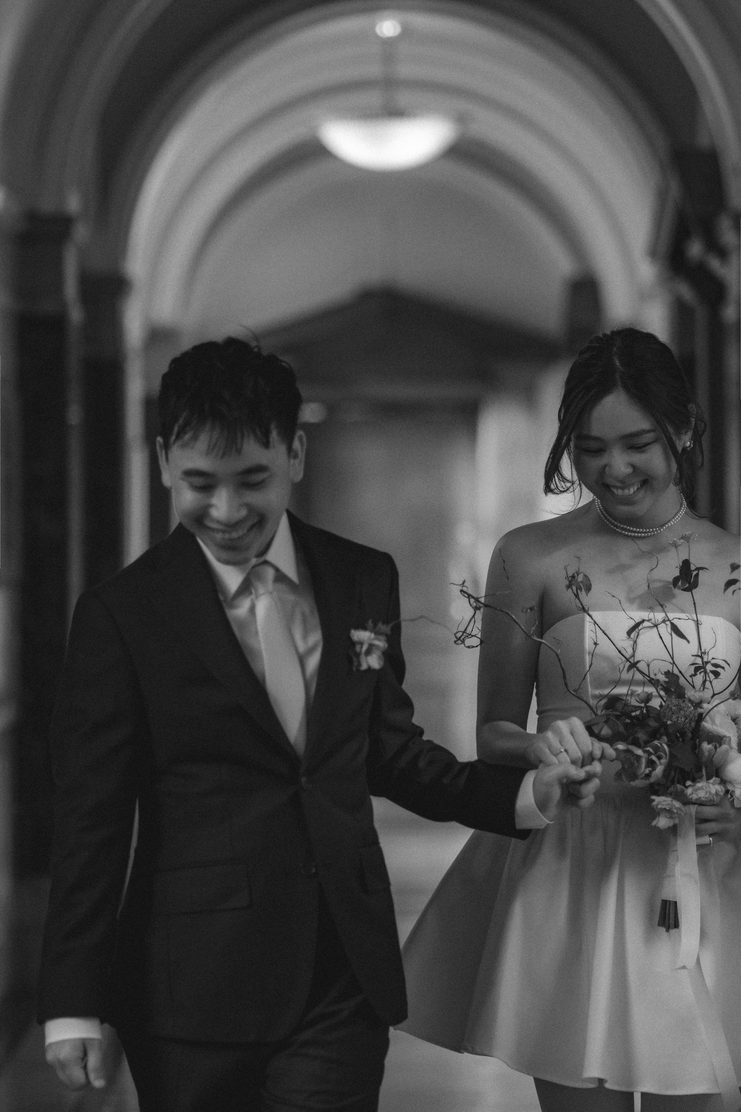 A black and white wedding photo series showing intimate moments between a couple in a hallway with arches.