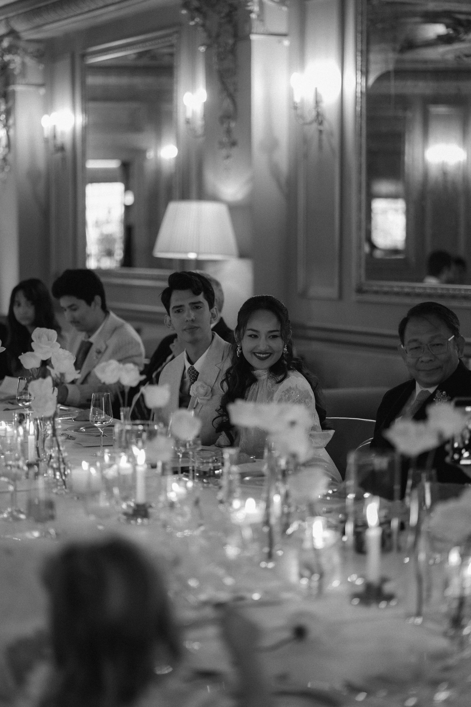 Black and white photo of people seated at an elegant candlelit dining table in a formal restaurant setting.