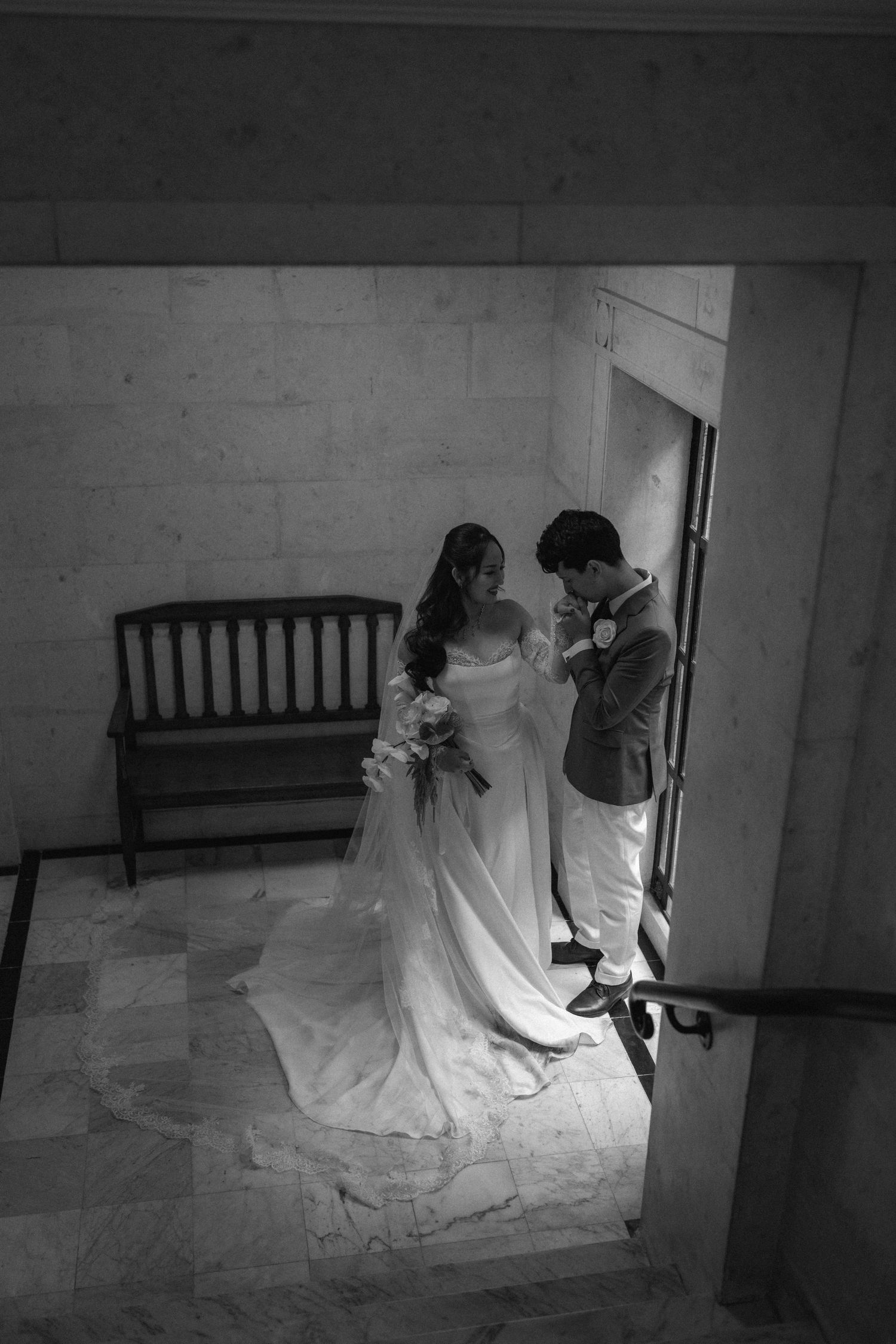 Black and white photo of bride and groom sharing a tender moment in an elegant marble hallway on their wedding day.