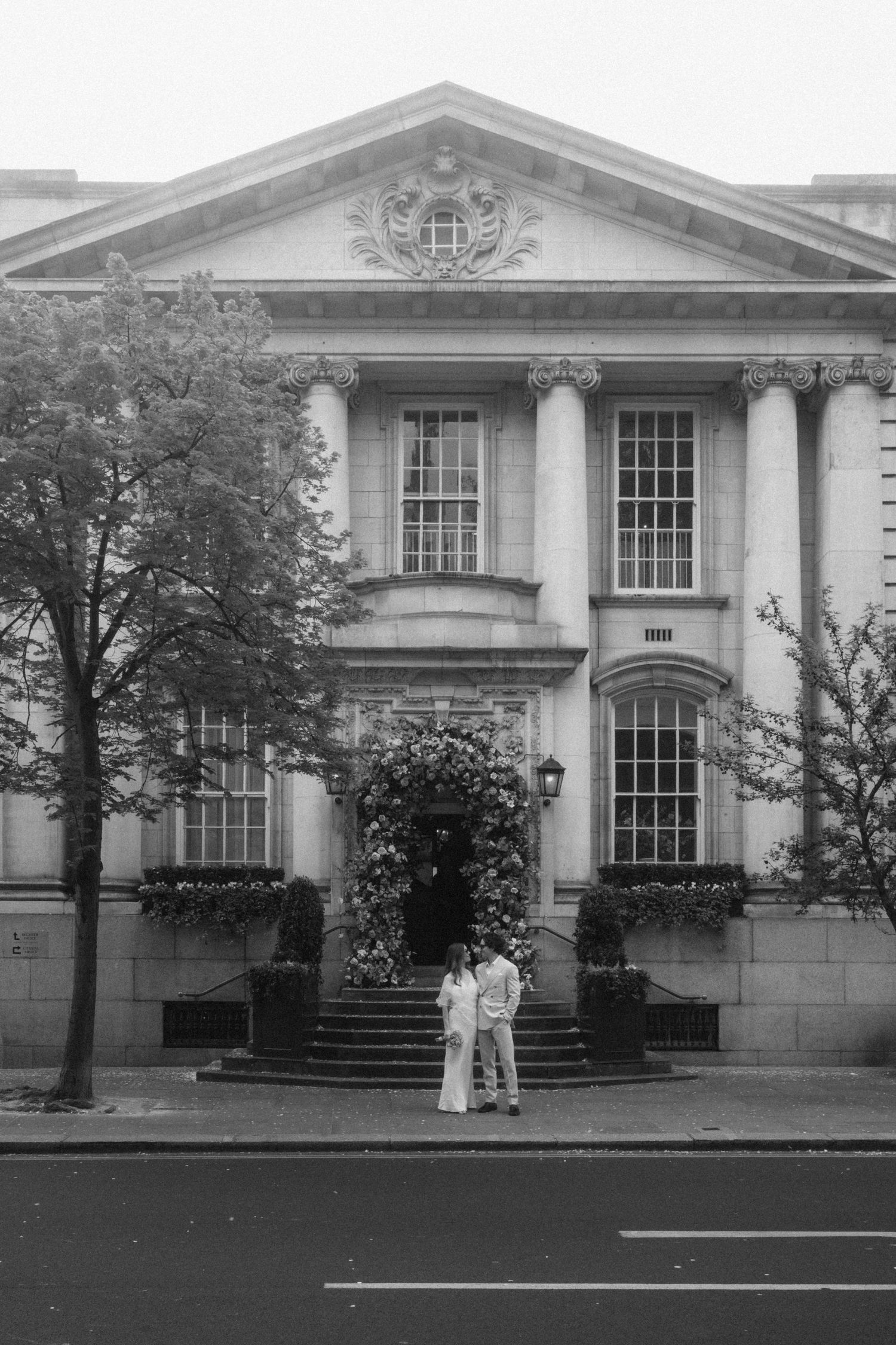 Couple standing on steps of grand neoclassical building with columns and ornate facade, black and white photo.