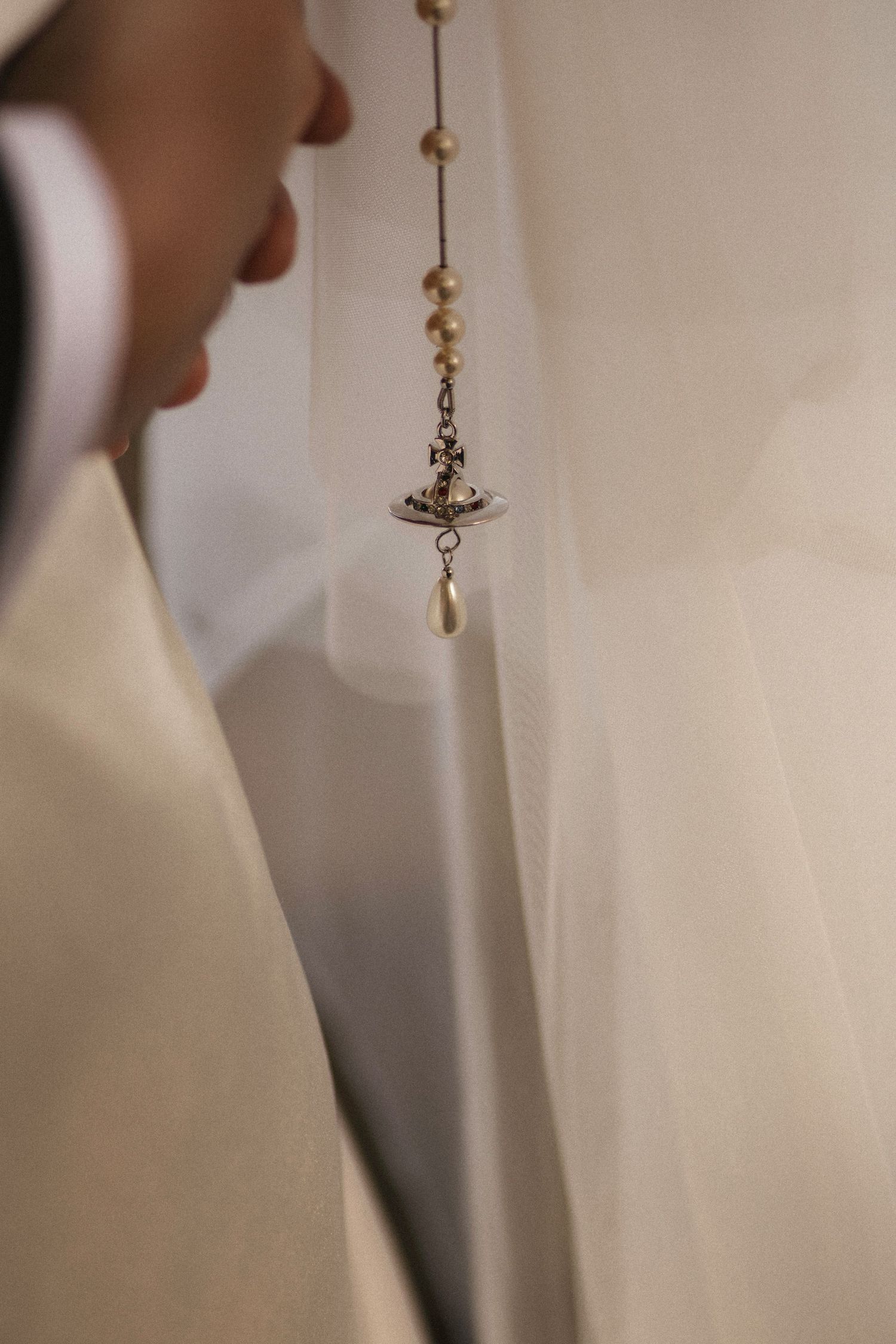 Close-up of an elegant pearl and crystal pendant necklace draped over a white wedding veil.