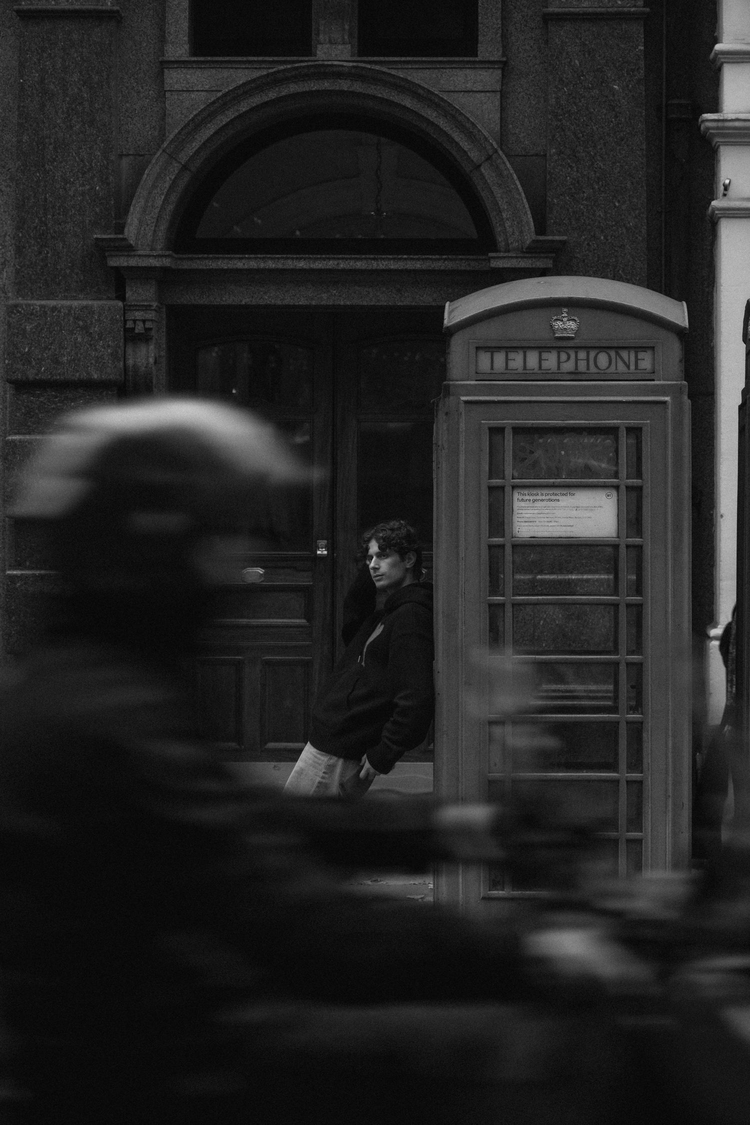 A moody black and white street scene with a classic British telephone booth and blurred motion in London.