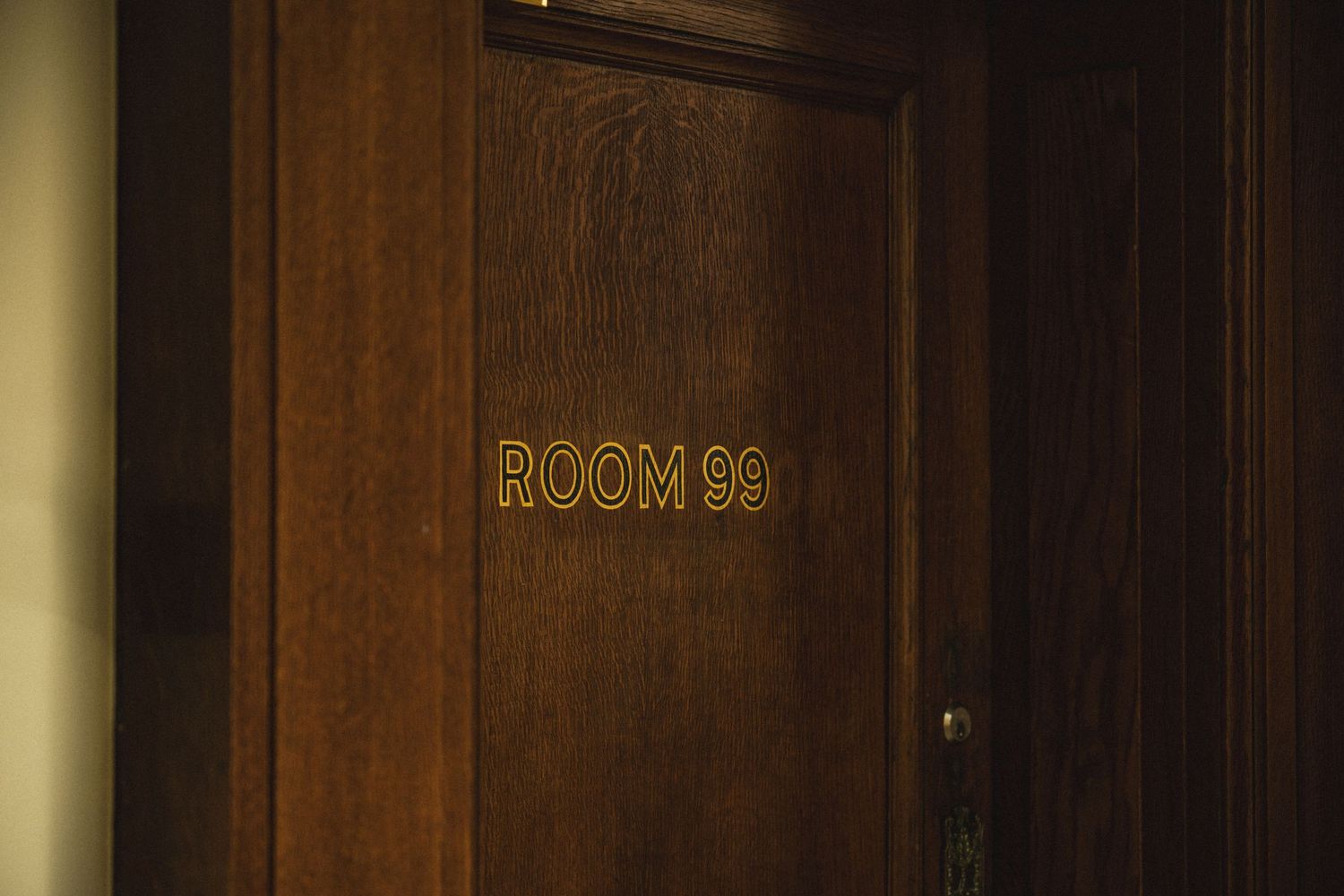 A modern office hallway with wooden paneled walls and glass doors showing 'Room 90' signage.