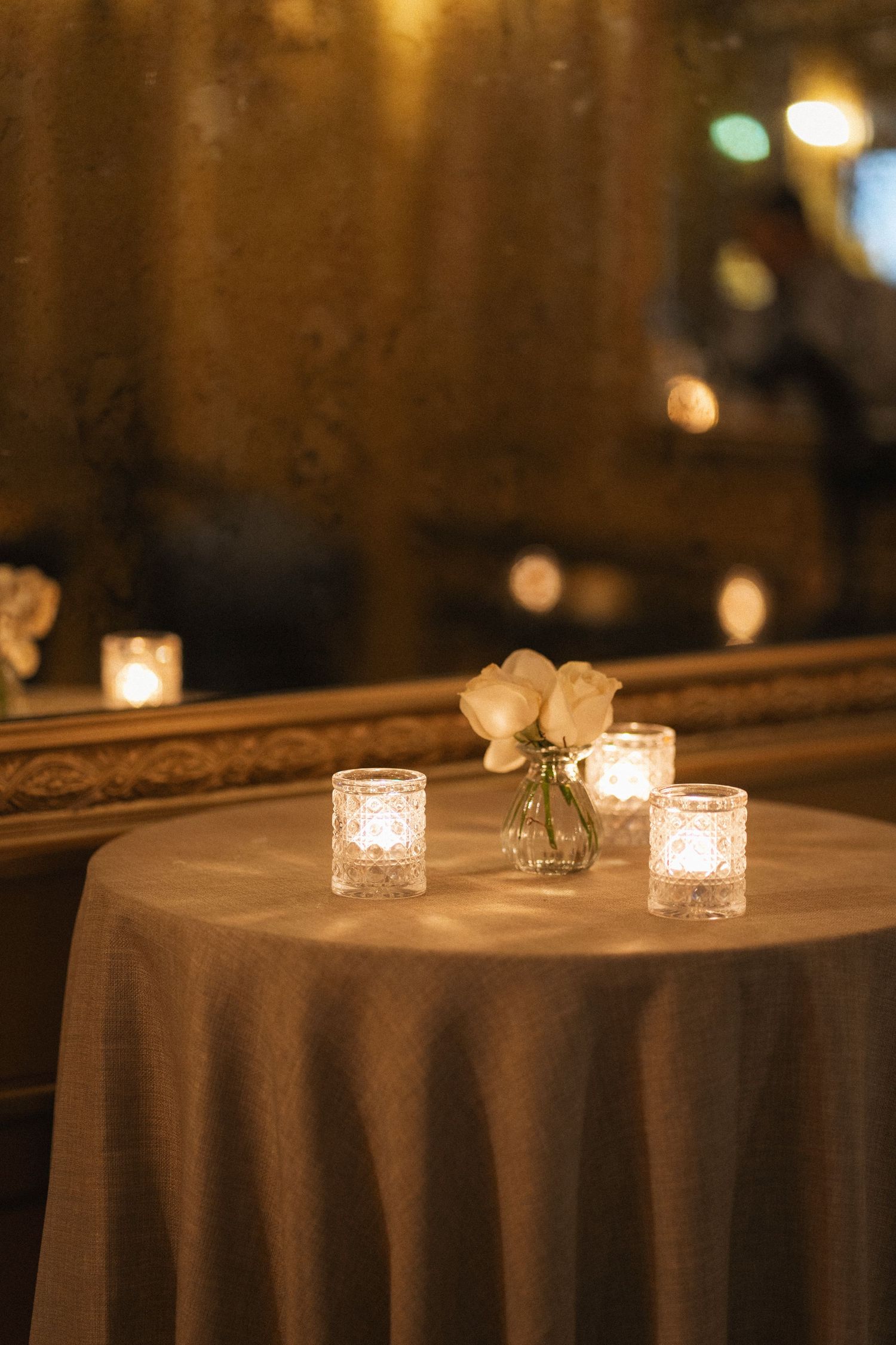 Glowing votive candles create romantic ambiance on round tables covered with white tablecloths at an evening event.