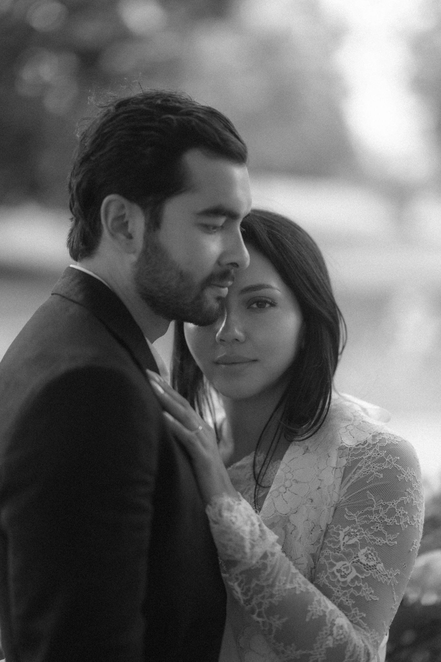 Black and white portrait of a couple in wedding attire sharing an intimate moment outdoors.