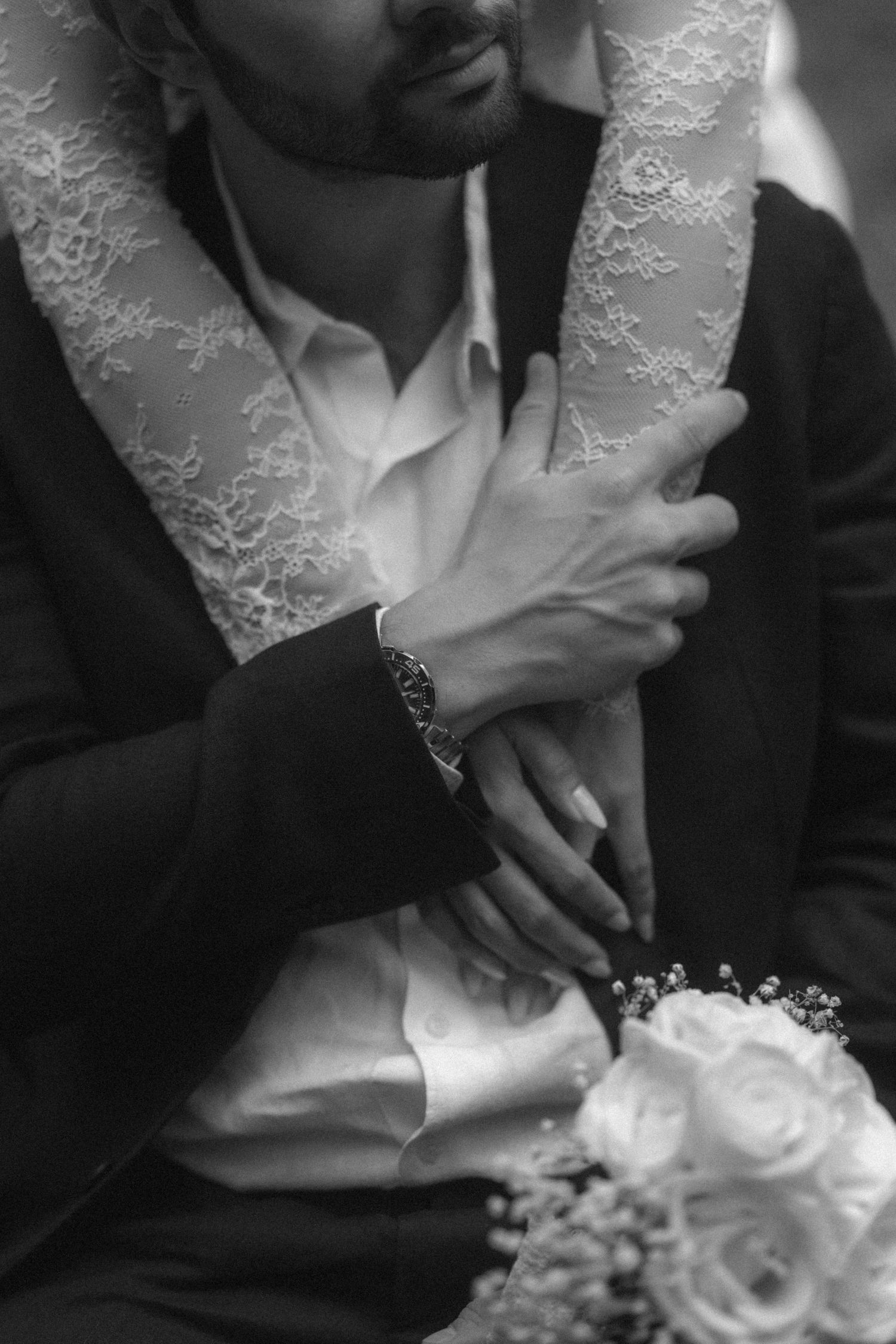 Black and white wedding photo of bride and groom holding hands, with lace veil and bridal bouquet of roses.