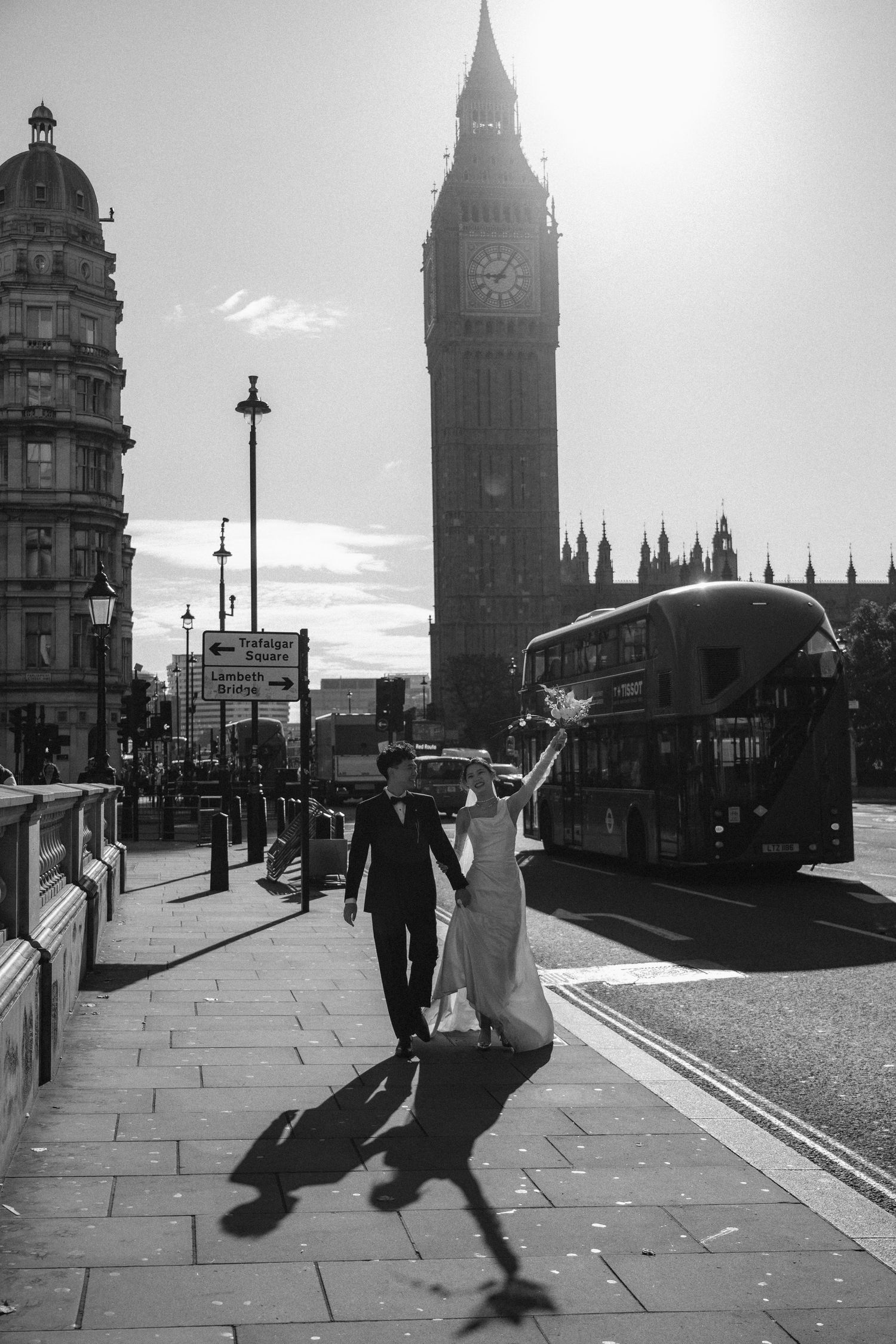 Black and white photo of a bride and groom walking near Big Ben and a red double-decker bus in London.