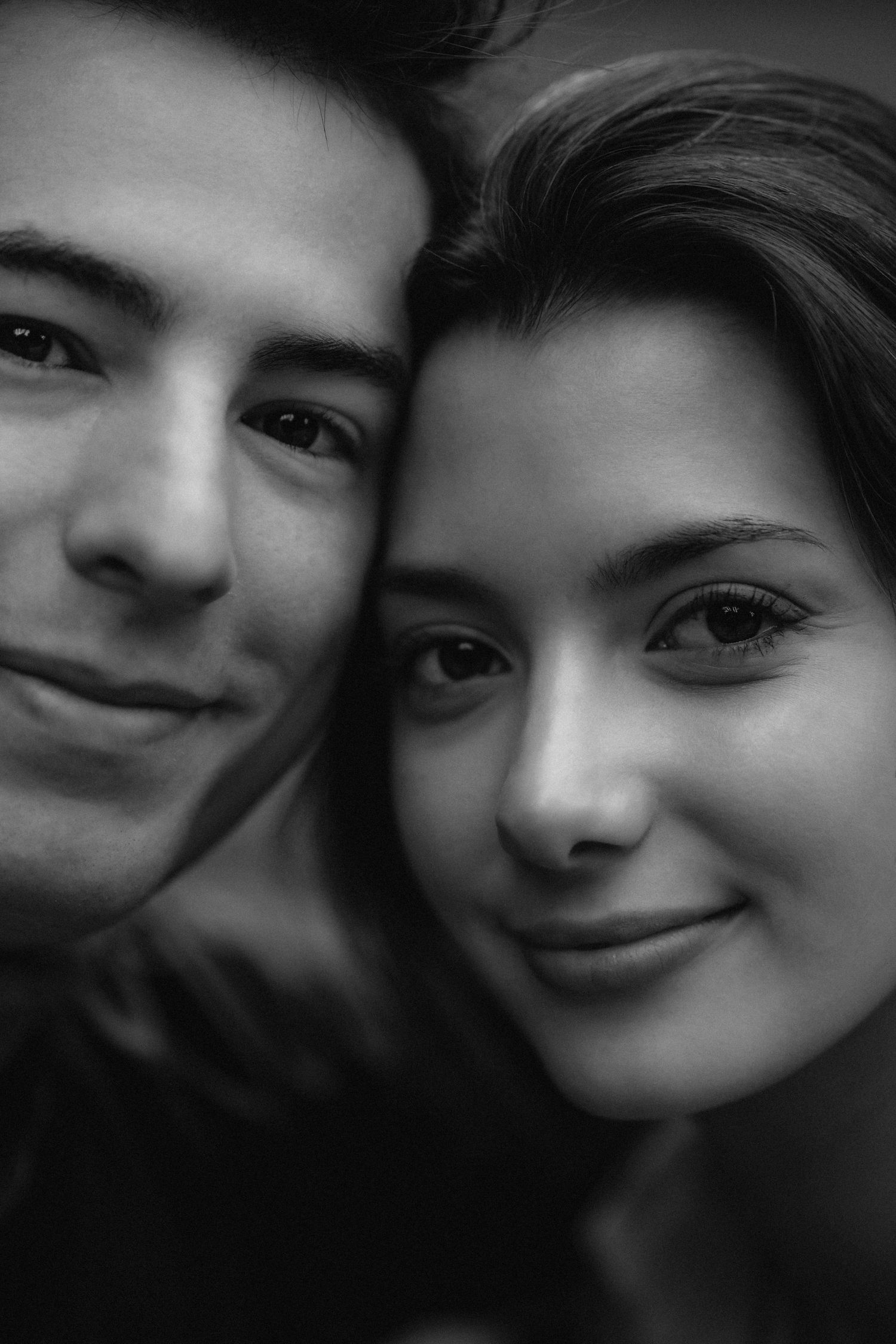 A black and white close-up portrait of a young couple smiling warmly at the camera.