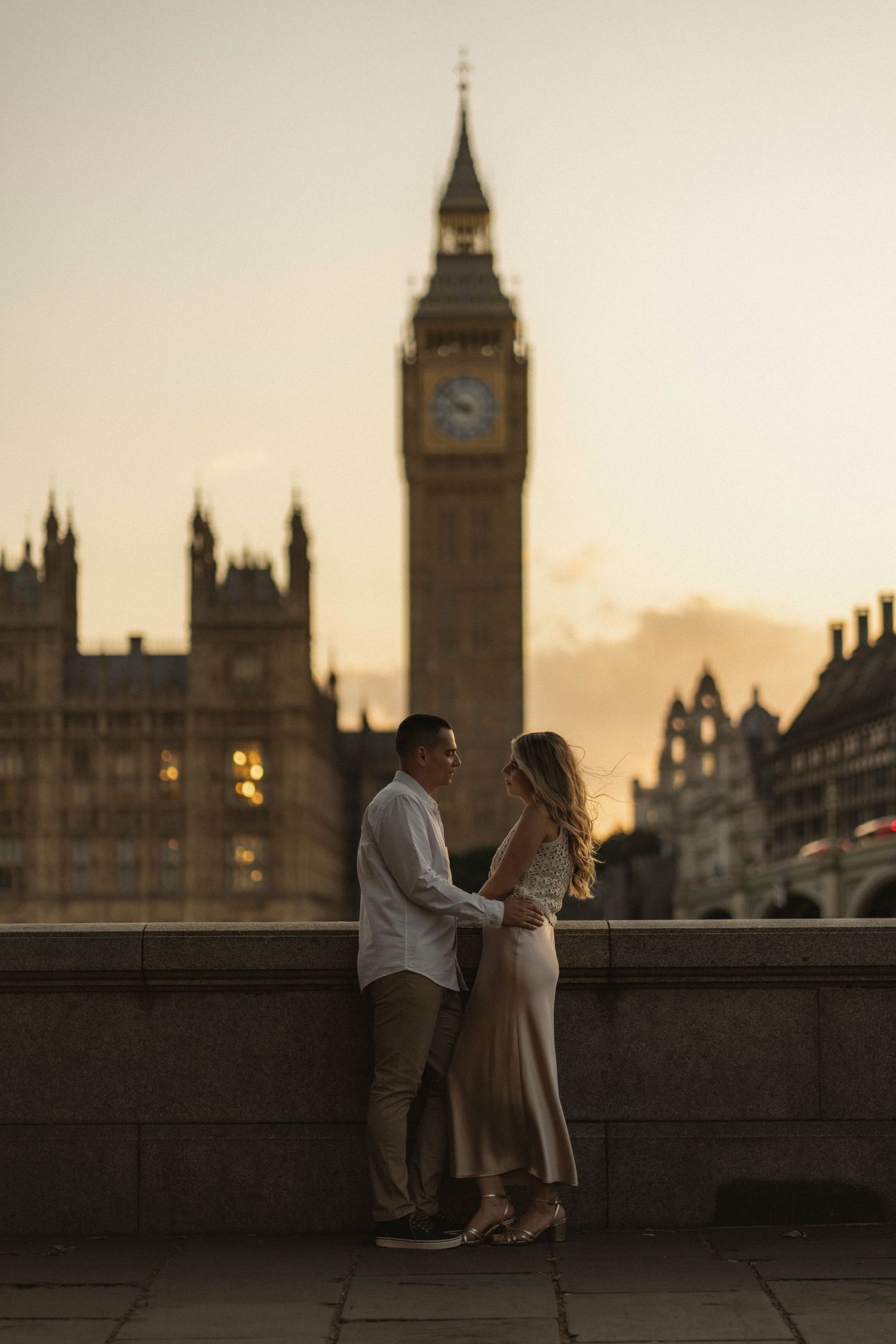 A romantic silhouette of a couple standing on Westminster Bridge at sunset with Big Ben and Parliament in the background.