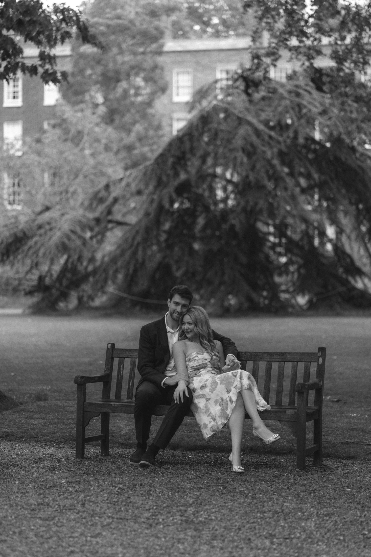 Black and white photo series showing a romantic moment between two people sitting on a park bench under a tree.
