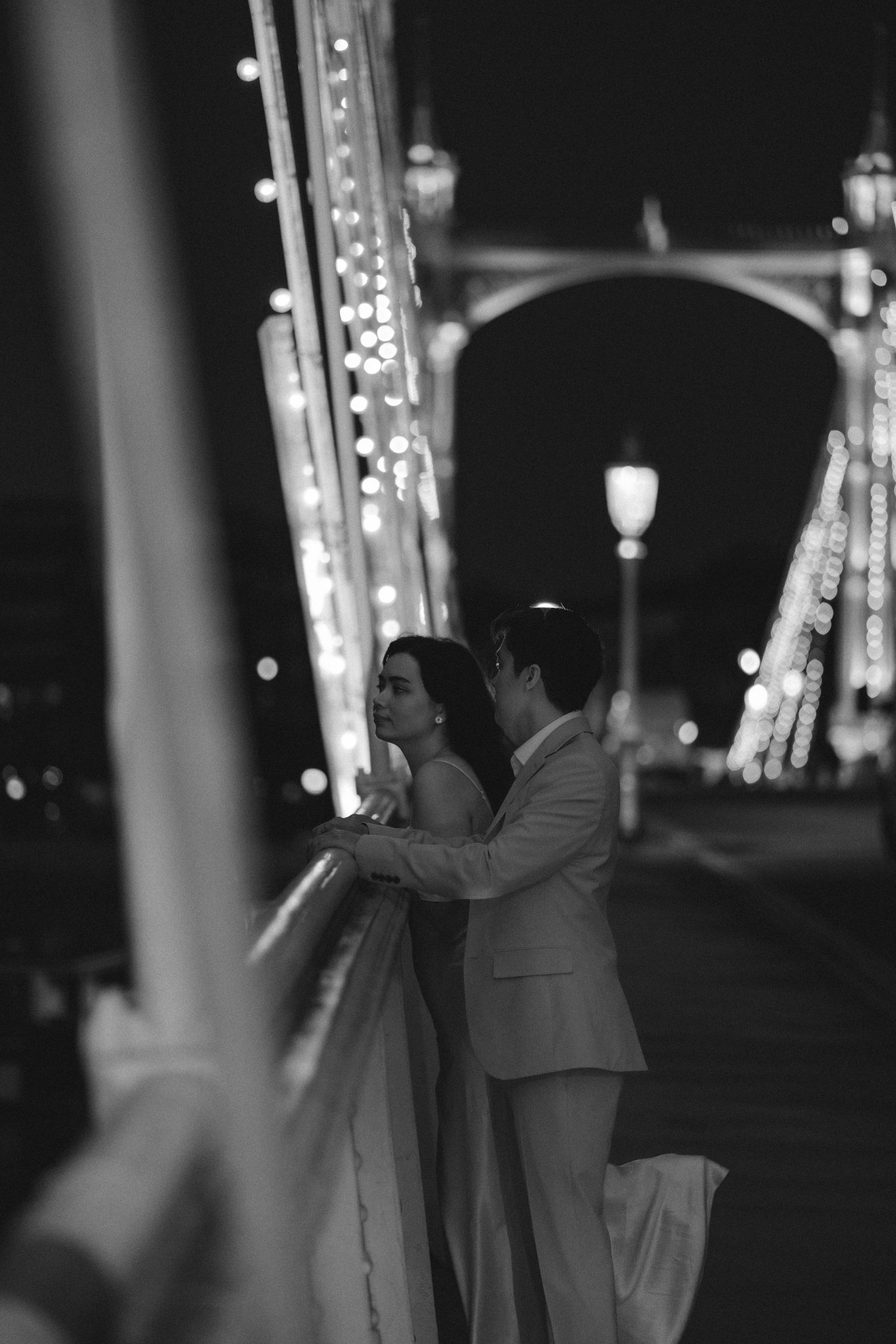 A romantic couple shares a dance under glowing lights in a black and white nighttime scene.
