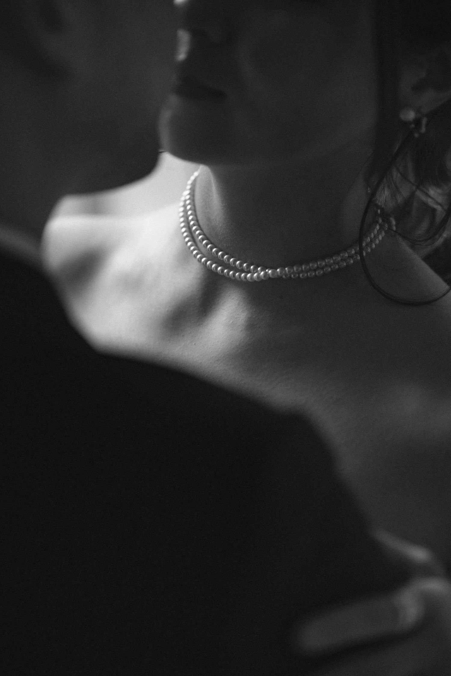 Black and white close-up of a woman wearing a pearl necklace, sharing an intimate moment with a partner.