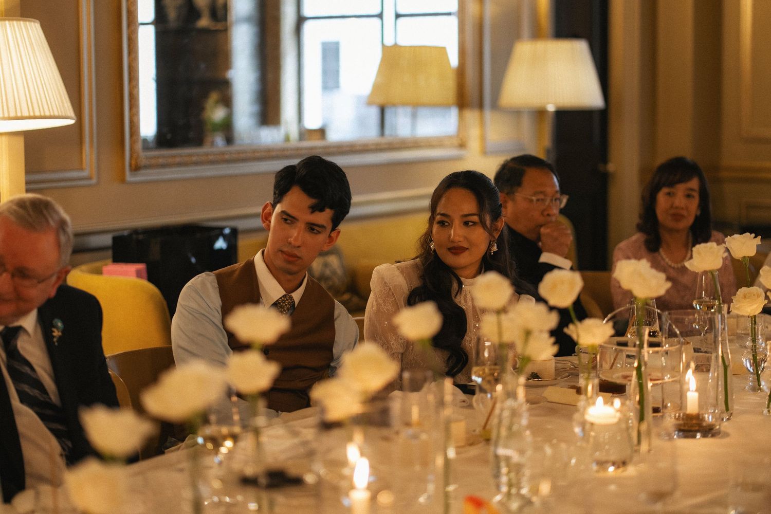 Guests smiling and laughing at an elegant wedding reception dinner with white roses and candles.