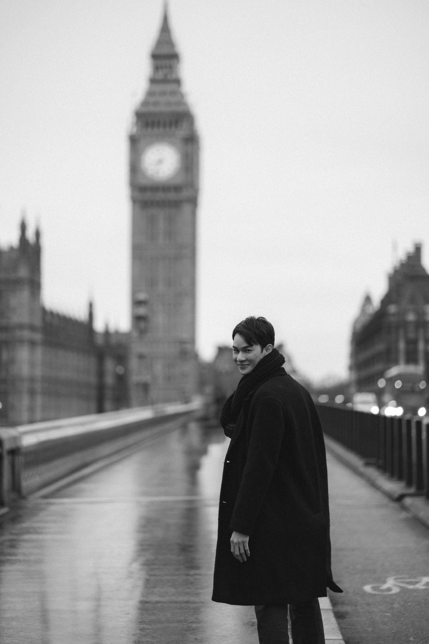 A person in a black coat walks across Westminster Bridge with Big Ben and London landmarks visible in black and white.