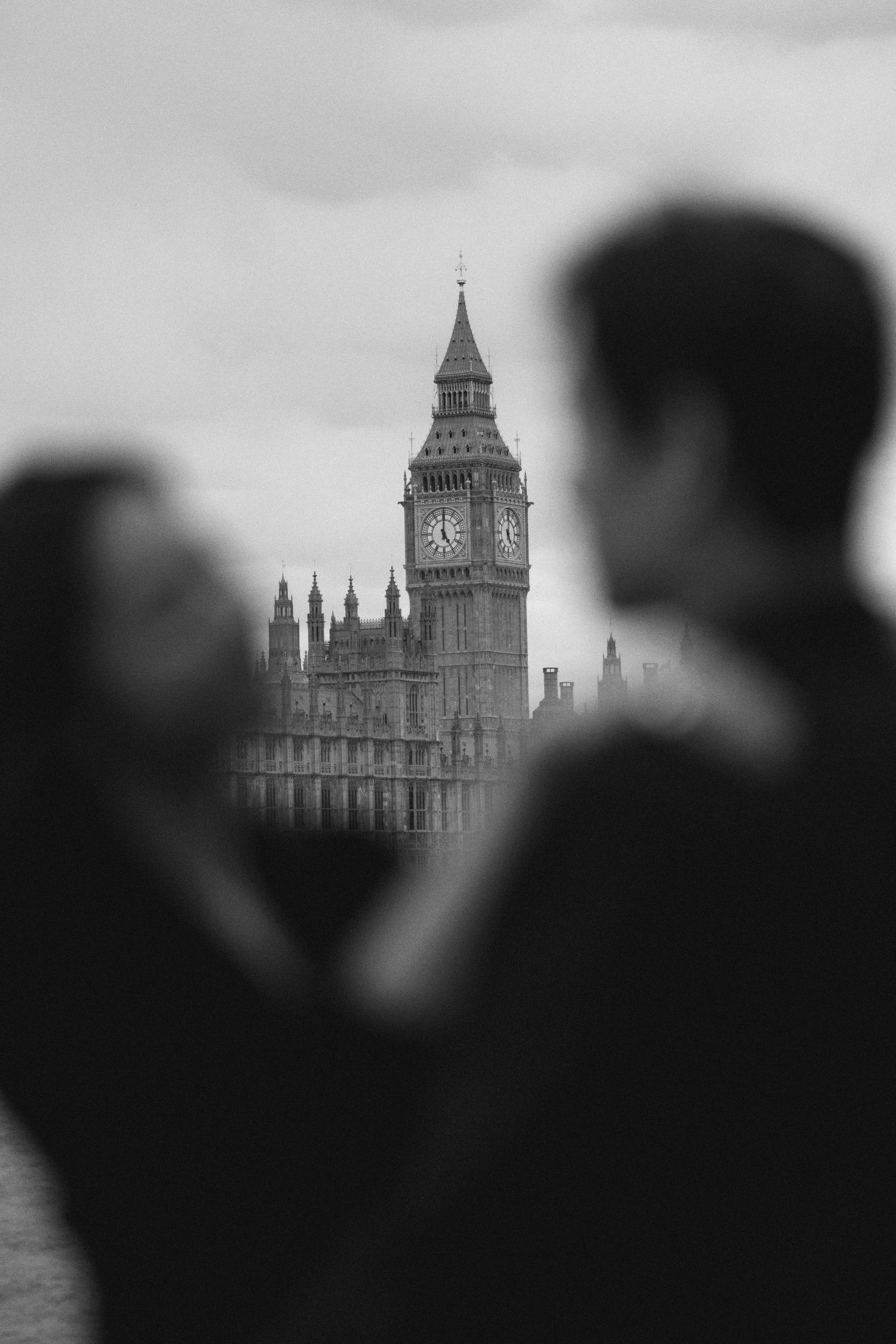 Silhouetted figures gaze at London's iconic Big Ben tower and Houses of Parliament in black and white.