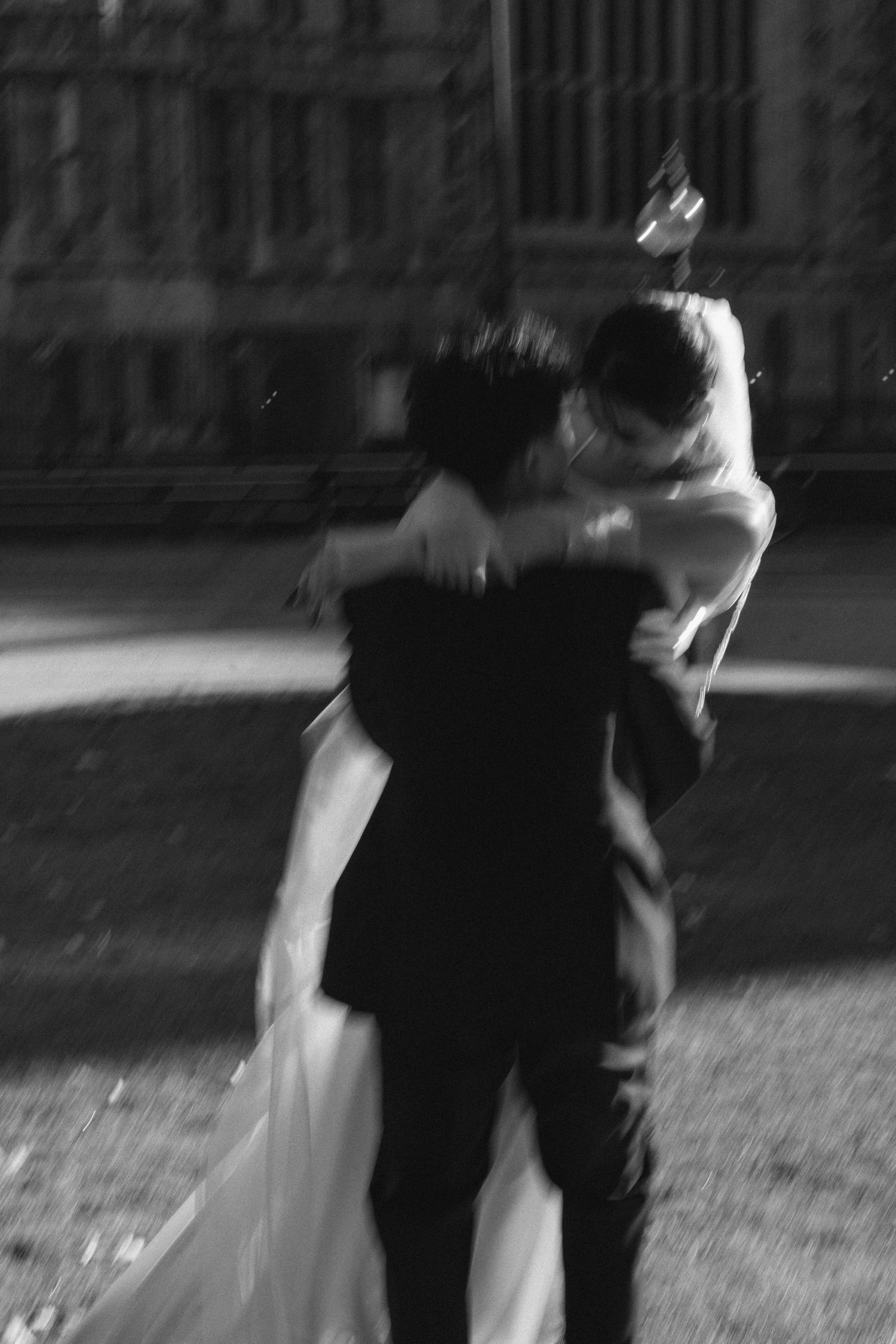 Black and white photo of a couple embracing in a wedding dance outdoors, captured with artistic motion blur.