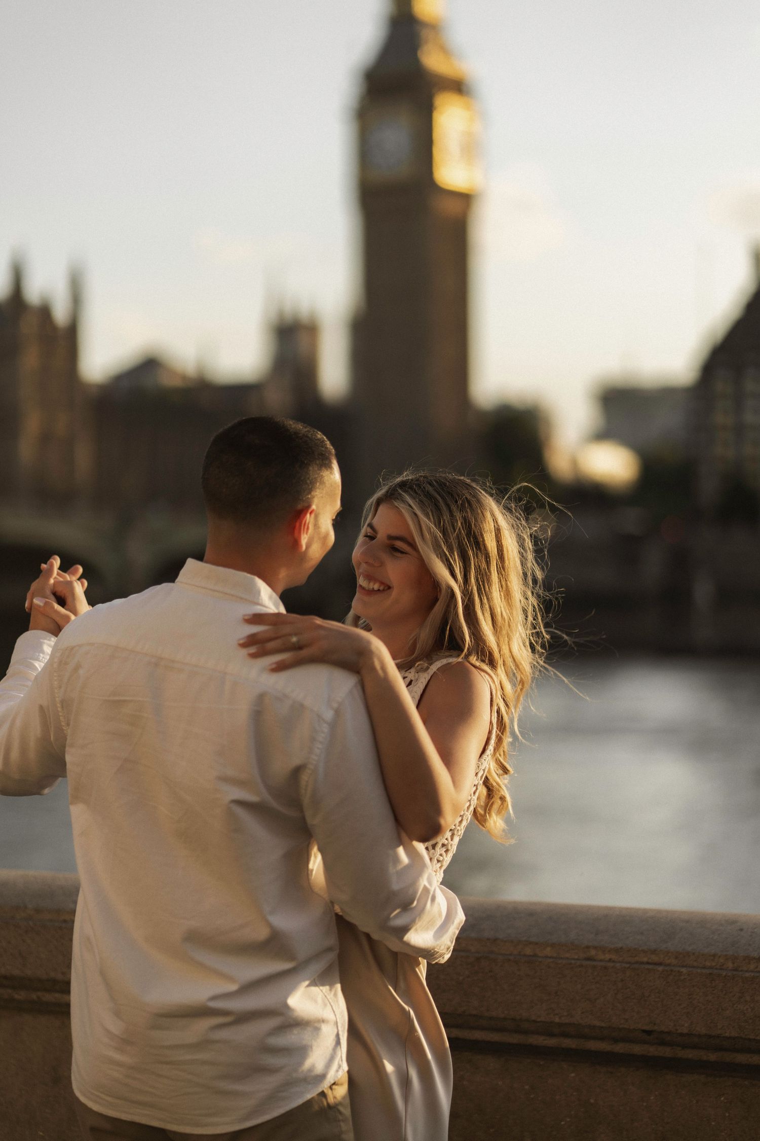 A romantic couple shares an intimate moment along the Thames River with London's Big Ben silhouetted in the background.