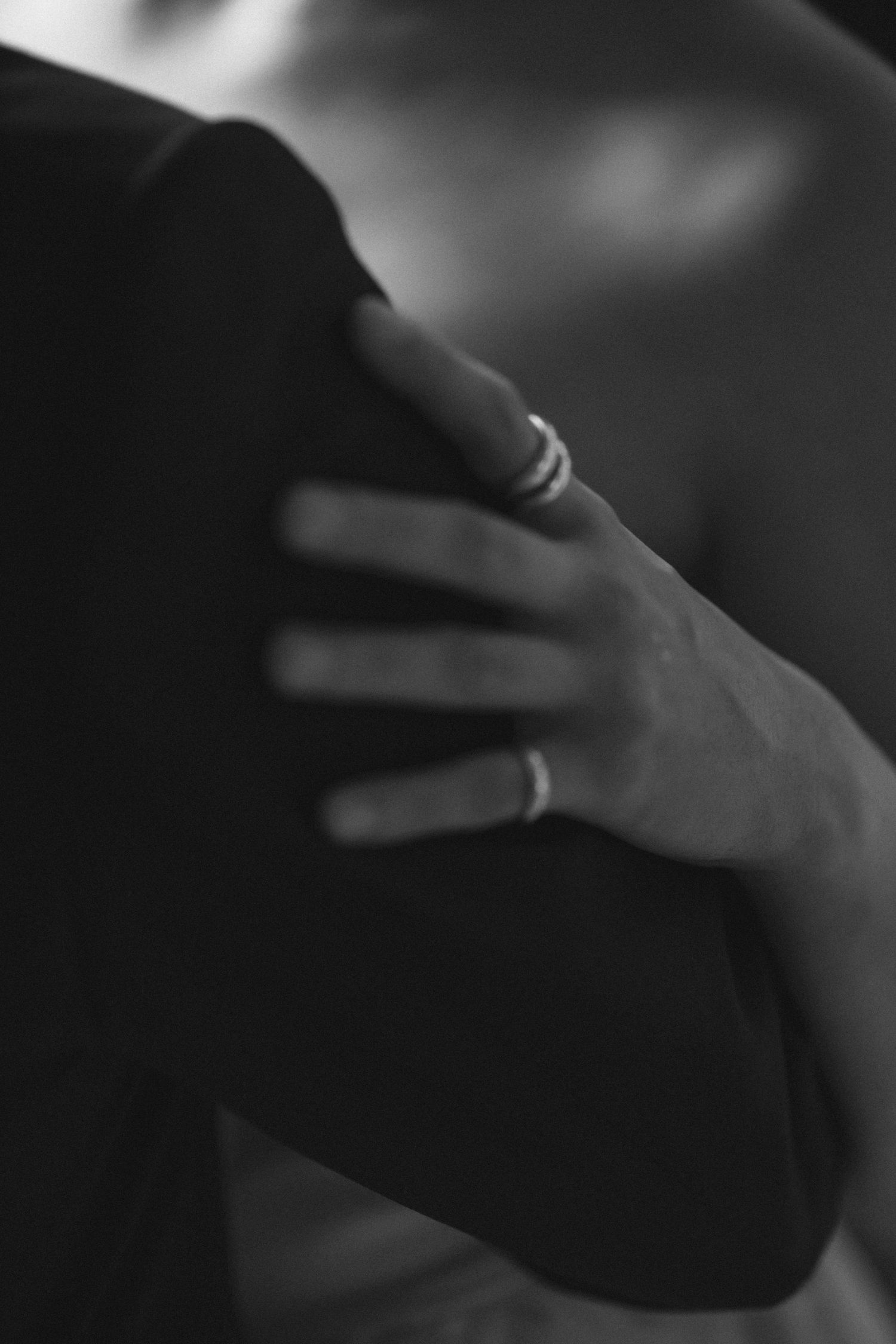 Black and white close-up of a hand with rings resting on a shoulder, evoking intimacy and elegance.
