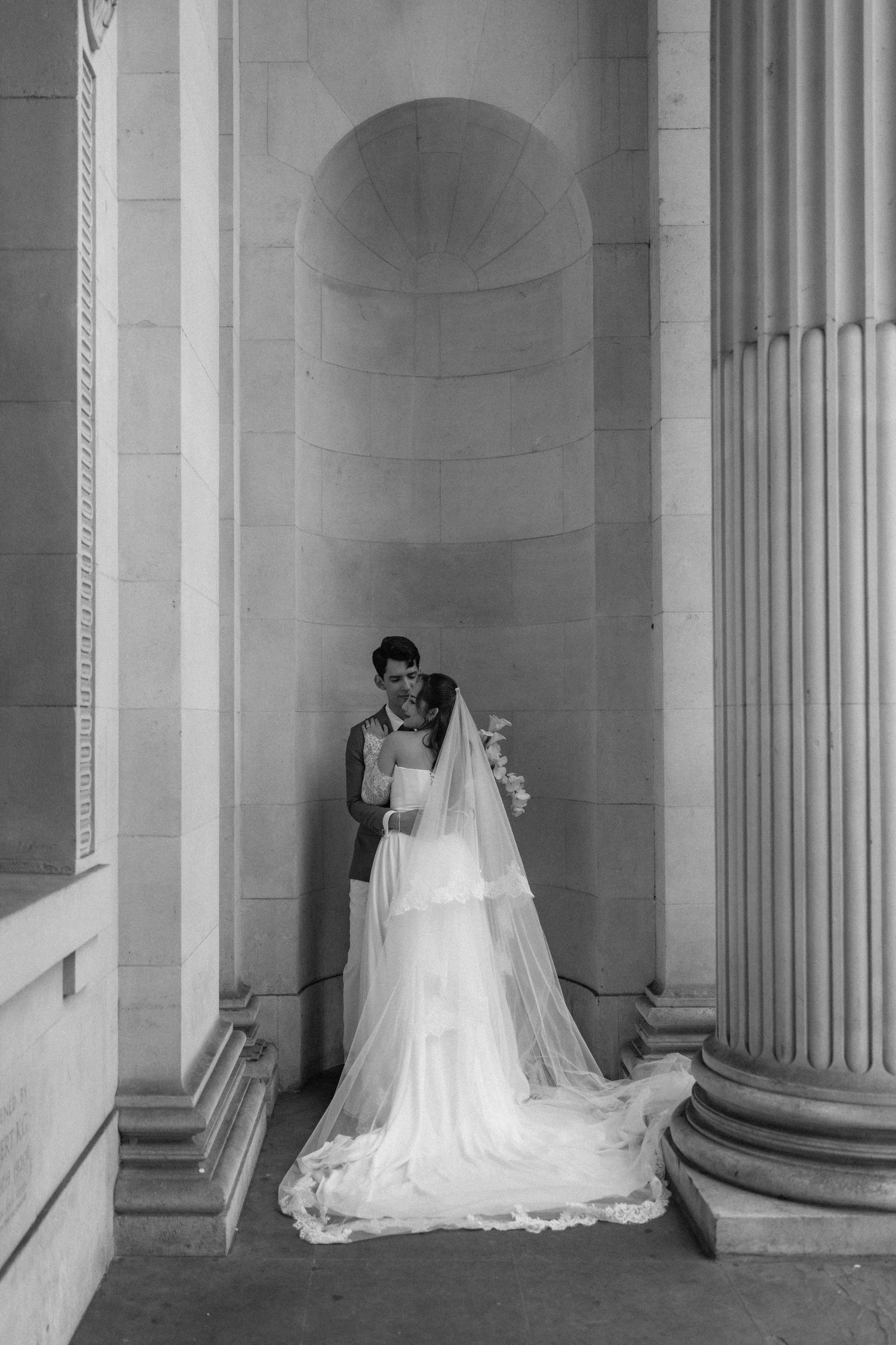 A series of four black and white photographs showing a white wedding dress displayed between classical columns.