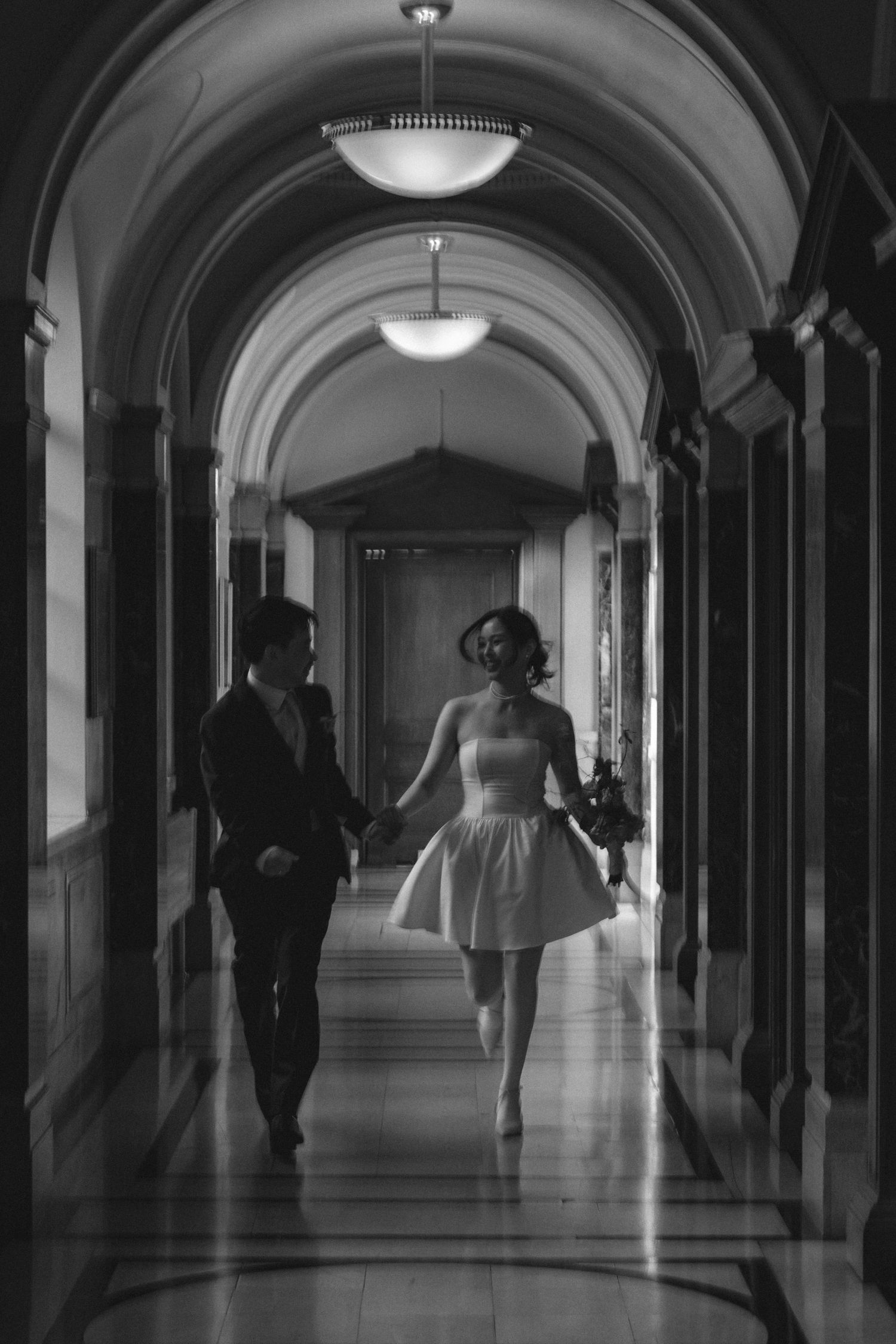 Silhouetted figures walk through a dimly lit arched hallway with dramatic lighting and shadows.