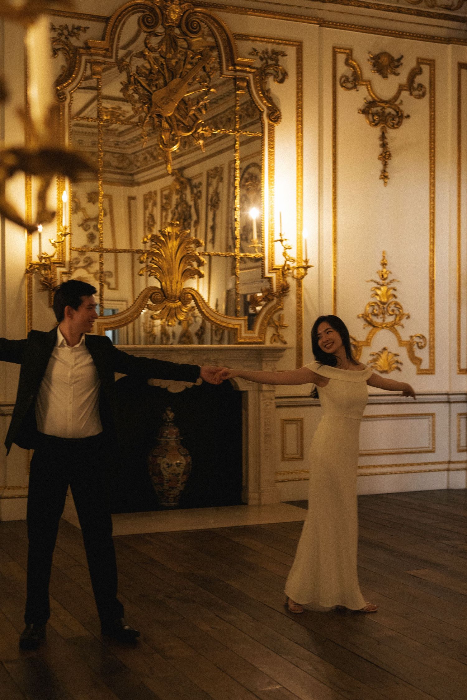 A couple dances gracefully in an ornate baroque ballroom with gilded walls and chandeliers.