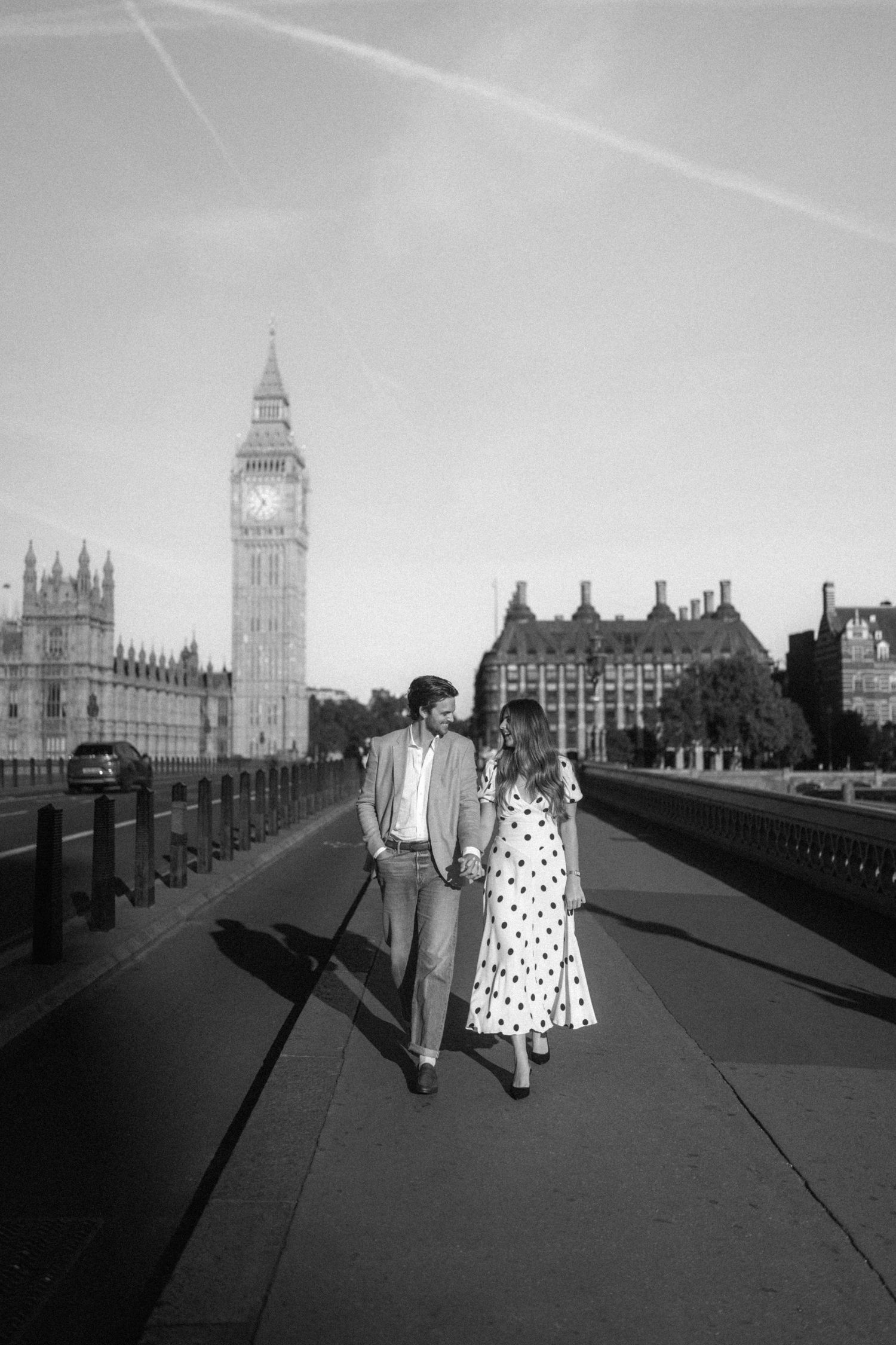 Black and white photo of a couple holding hands on Westminster Bridge with Big Ben in the background, London.