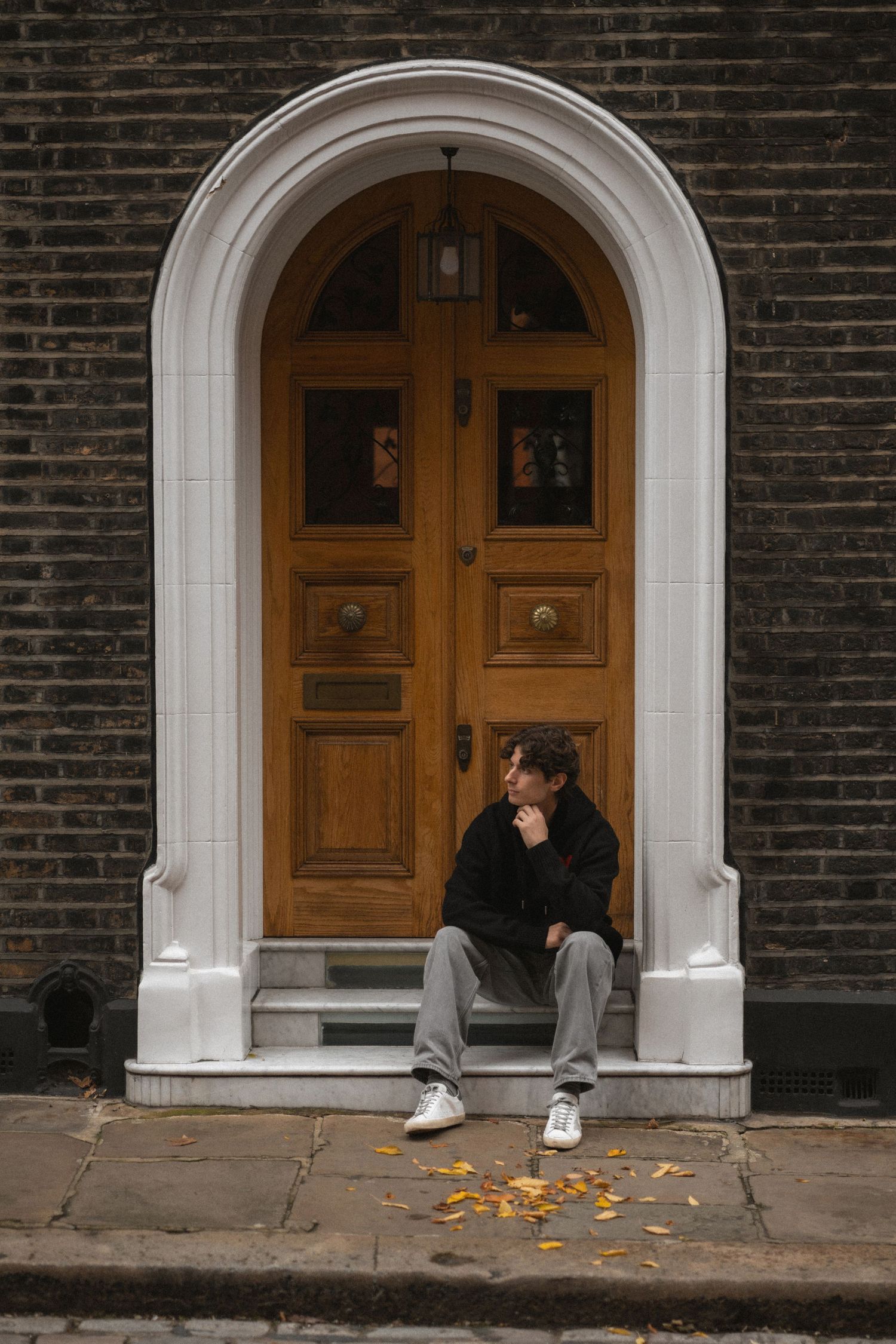 A sequence of four photos showing someone sitting alone on a doorstep of a brick building with white archway entrance.